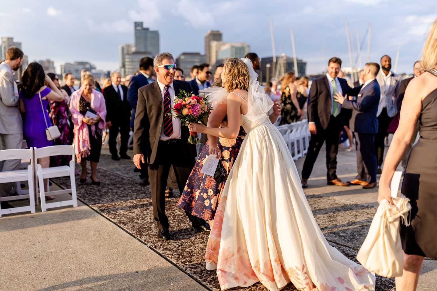 A wedding celebration at an outdoor waterfront venue with guests mingling at sunset.