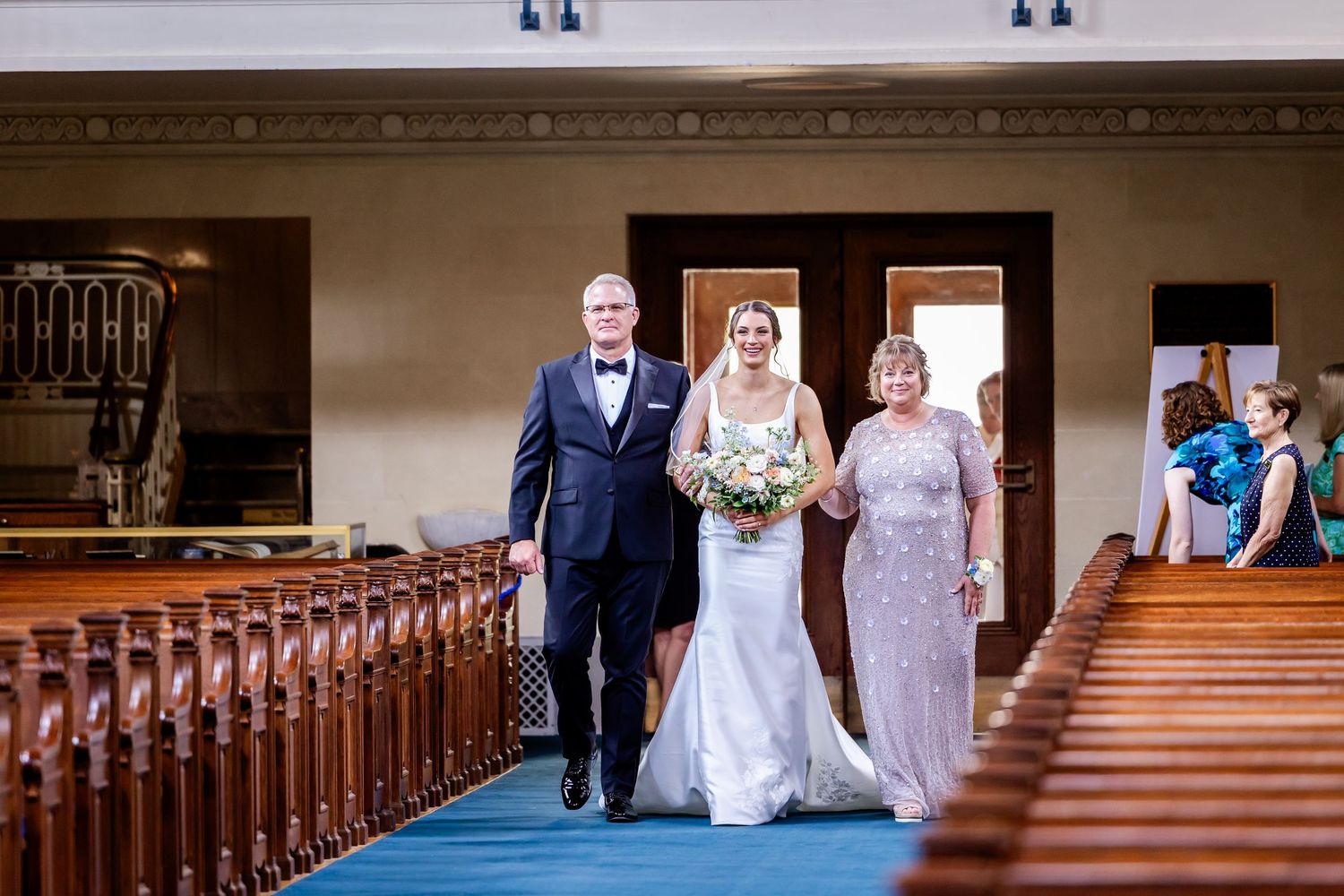 Wedding ceremony procession inside a traditional church with wooden pews and classic architecture.