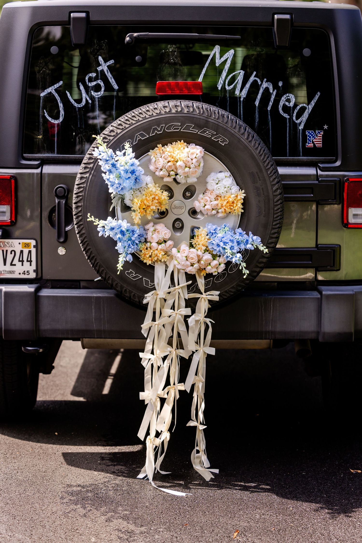 Just Married sign with floral decorations on spare tire of black Jeep vehicle.
