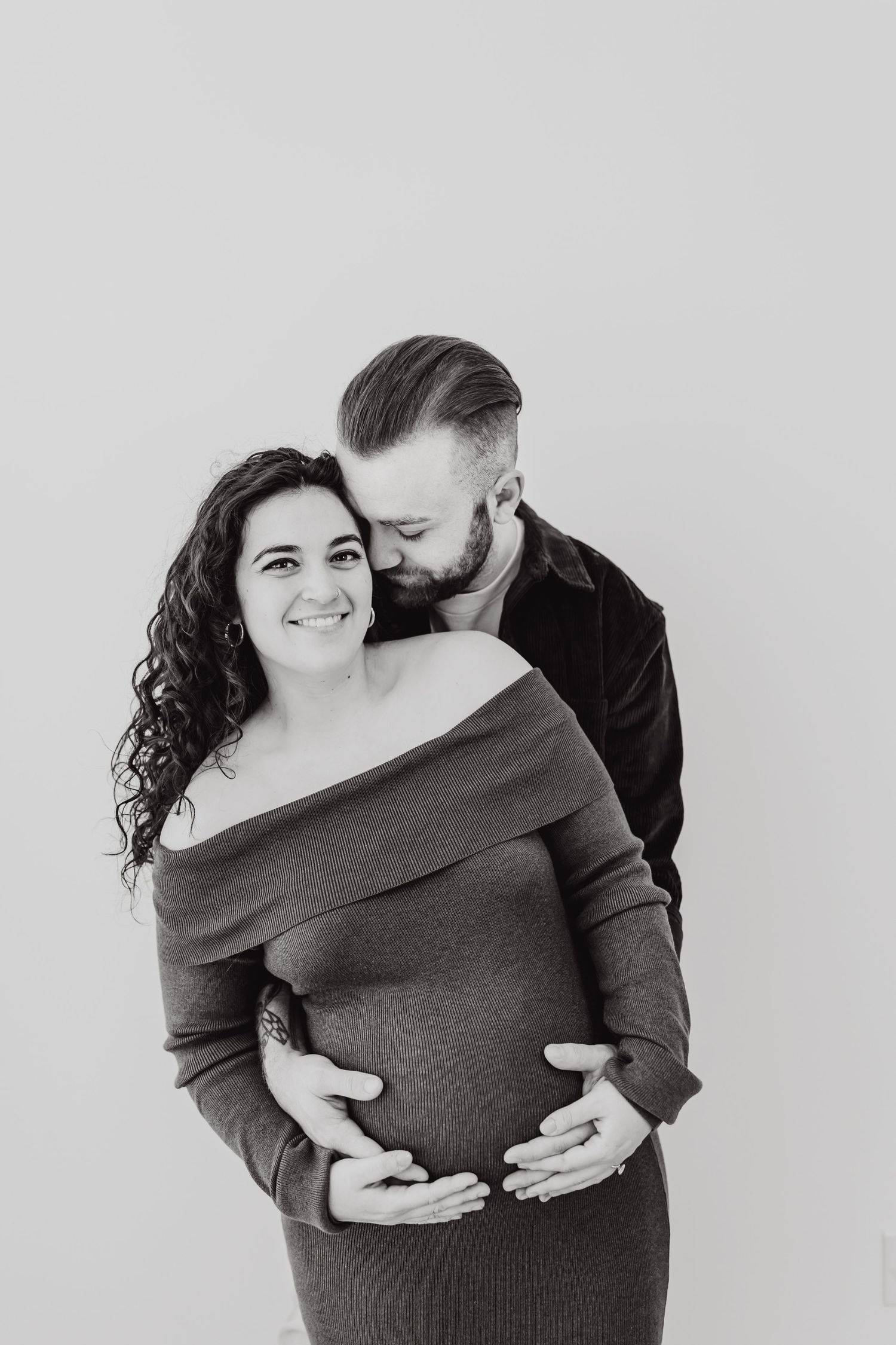 Black and white maternity portraits capturing tender moments between expecting couple.