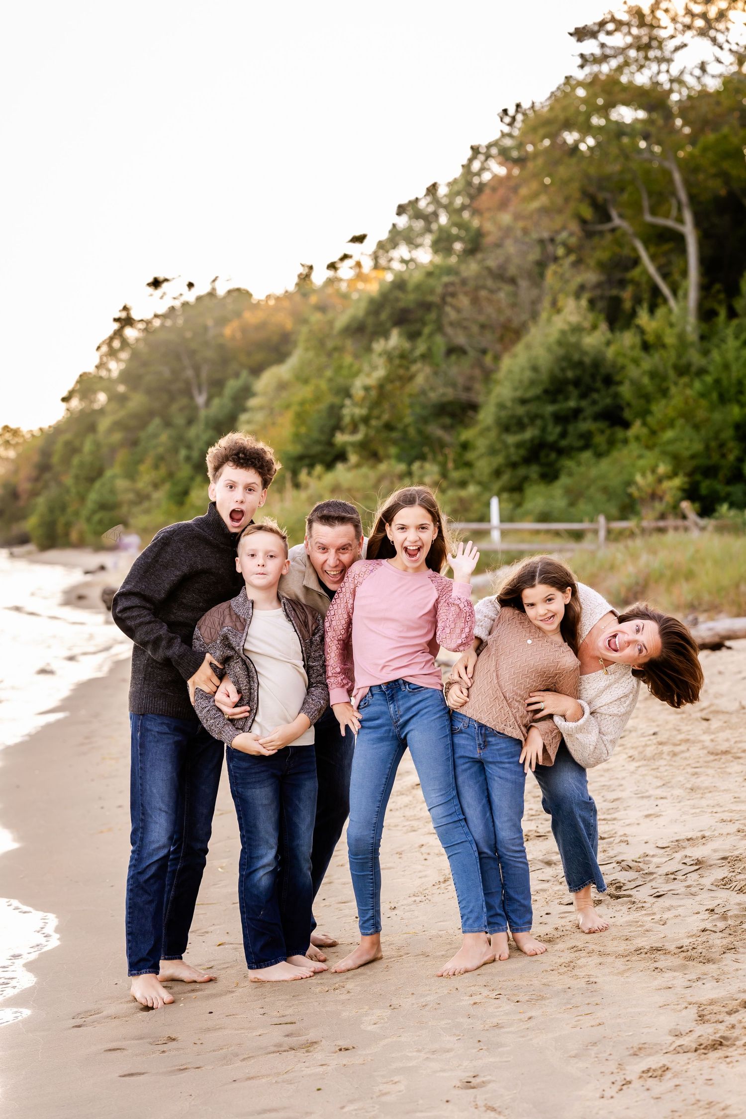 Playful group poses while bending forward on sandy beach at sunset.
