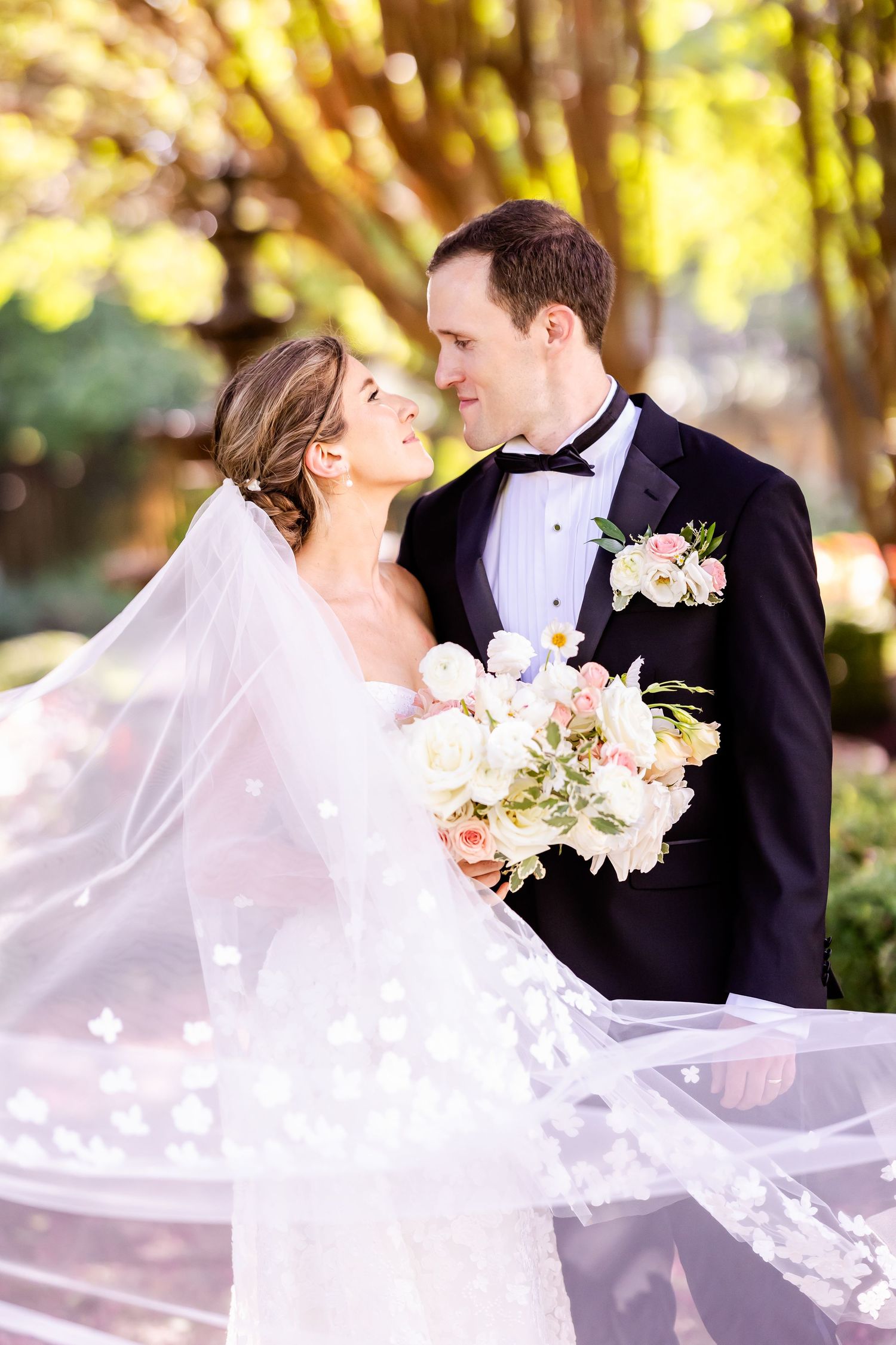 A romantic wedding moment captured with flowing veil against golden sunlit trees.