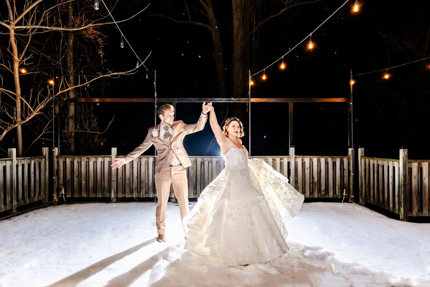 A romantic winter wedding ceremony takes place at night under string lights with snow-covered ground creating a magical ambiance.