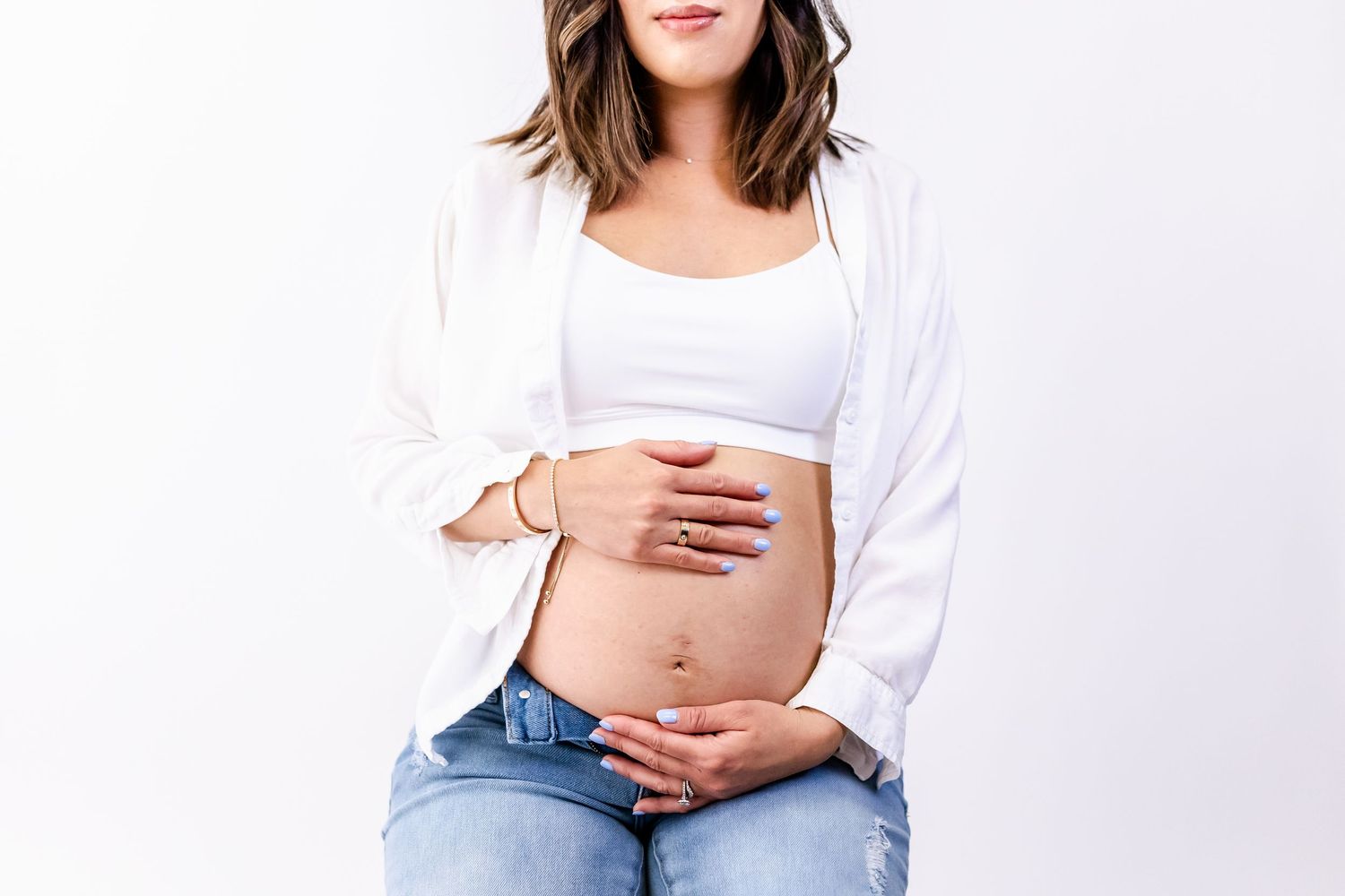 Close-up maternity photo showing pregnant belly with hands in white top and jeans.
