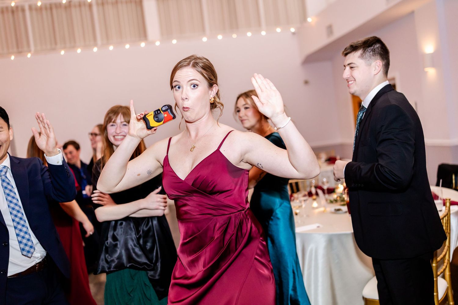 Wedding guests dance and celebrate on the dance floor under string lights at the reception.