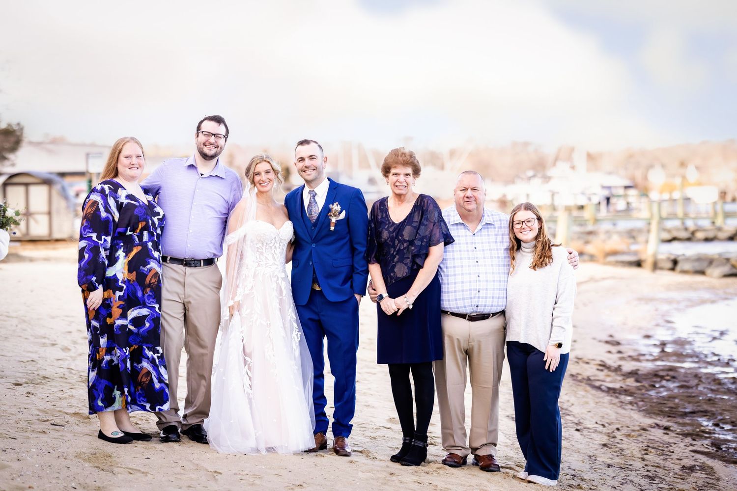 A group portrait on a beach with water and boats in the background.