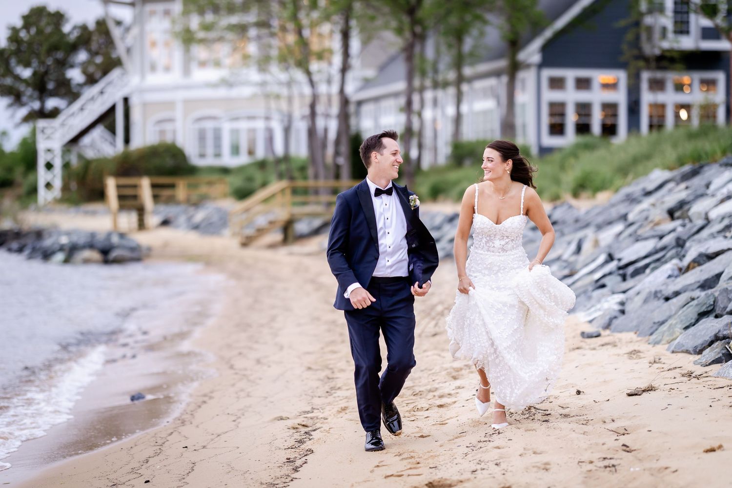 Wedding couple walking and posing along a scenic beach with rocks and water in the background.
