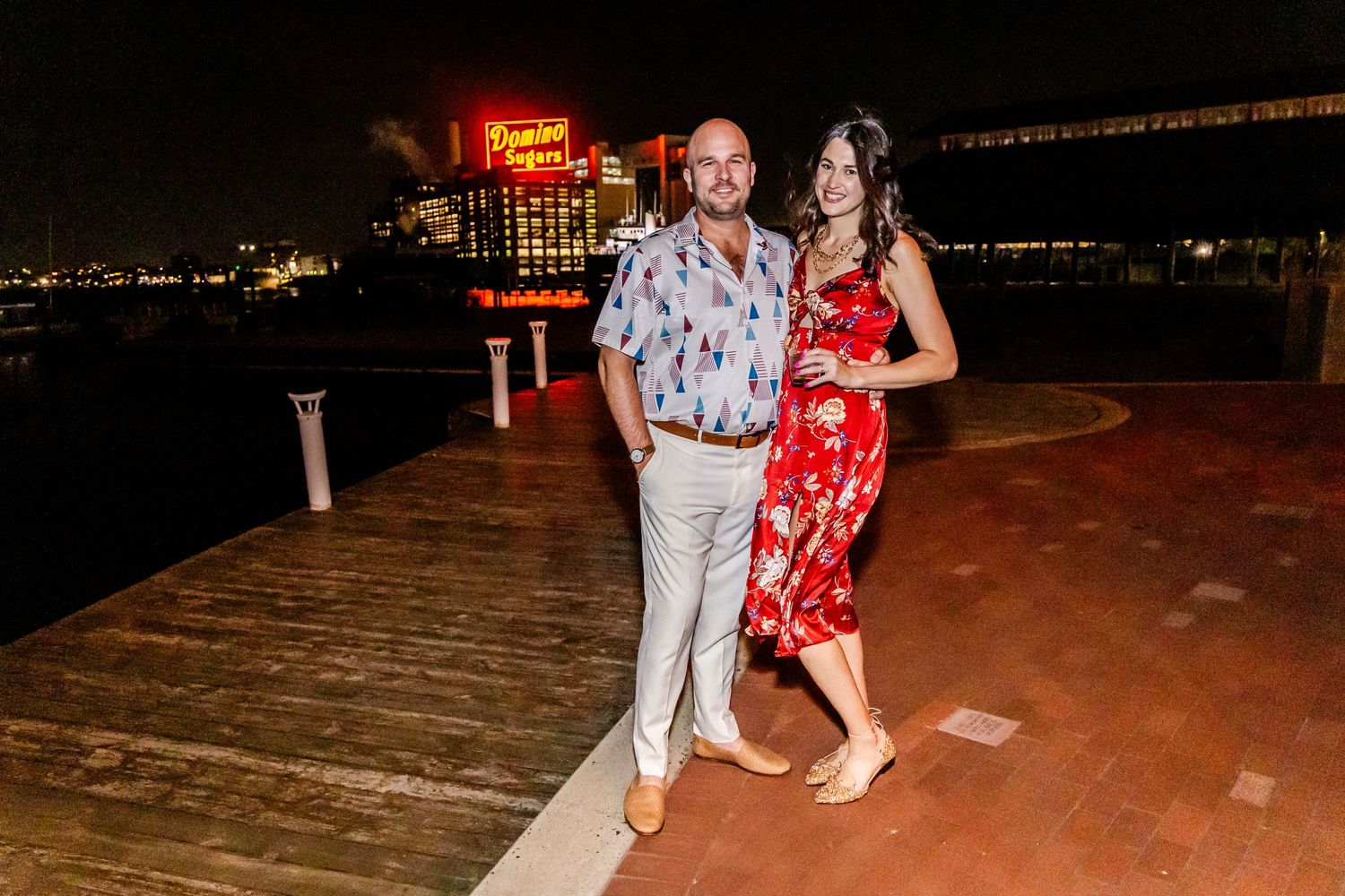 Couple dancing on a waterfront deck at night with glowing city lights in the background.