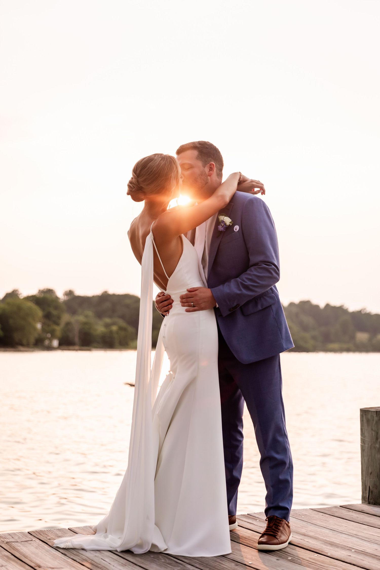 Two newlyweds share an intimate moment at sunset on a lakeside dock as golden light streams between them.