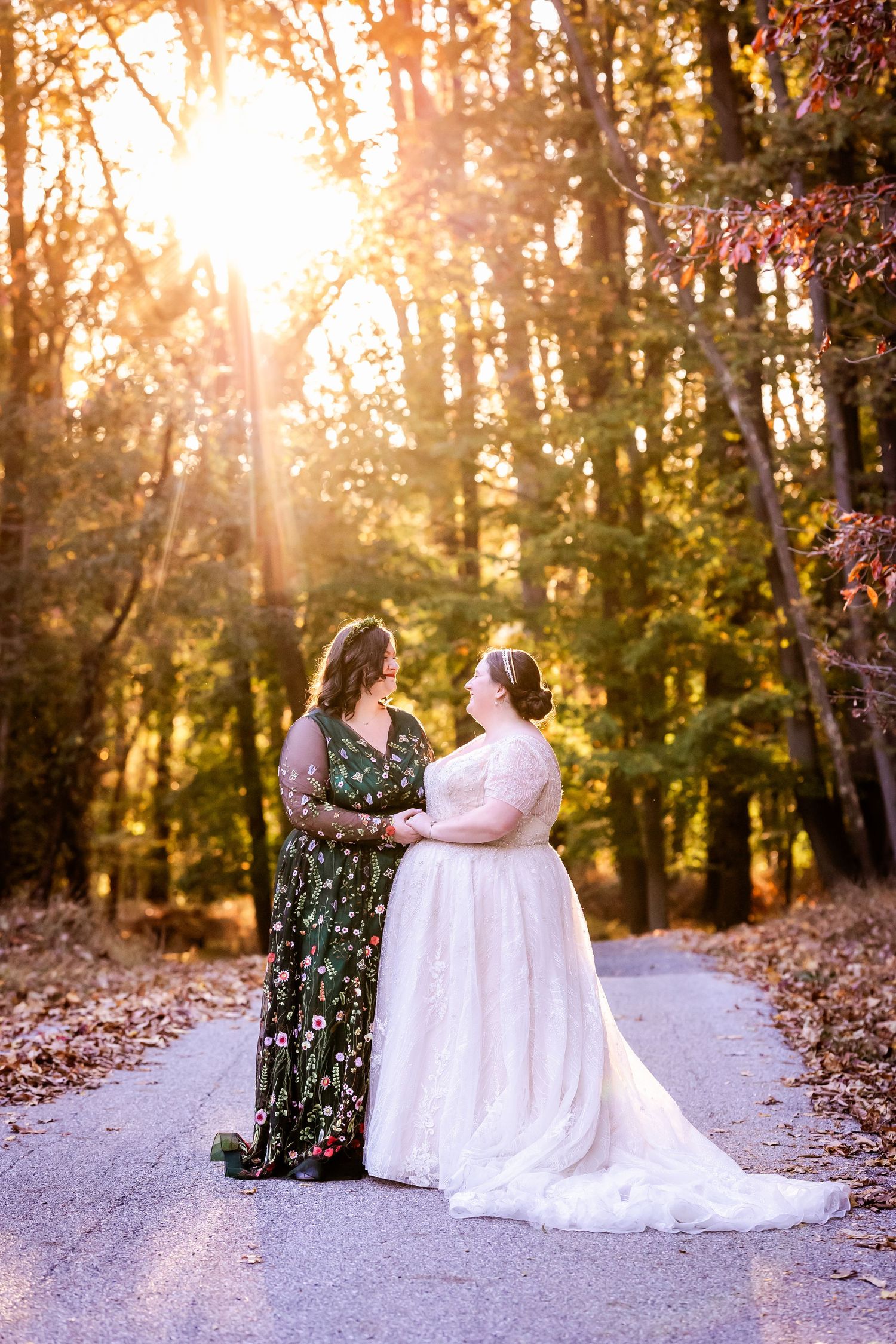 A magical sunset portrait of two people in wedding attire on a tree-lined path.