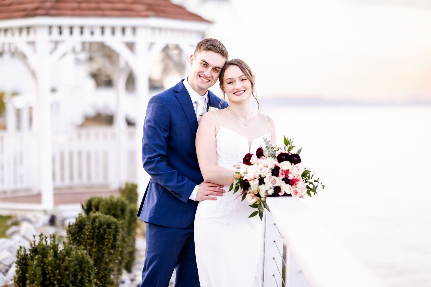 Elegant winter wedding portrait with burgundy and white floral bouquet against snowy backdrop.