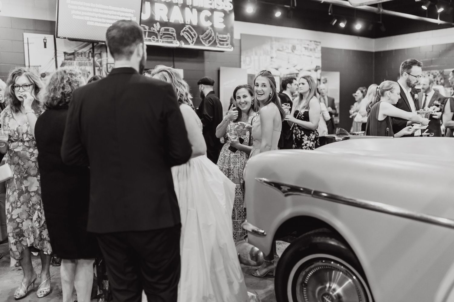 Black and white photo of wedding guests gathered around a classic car.
