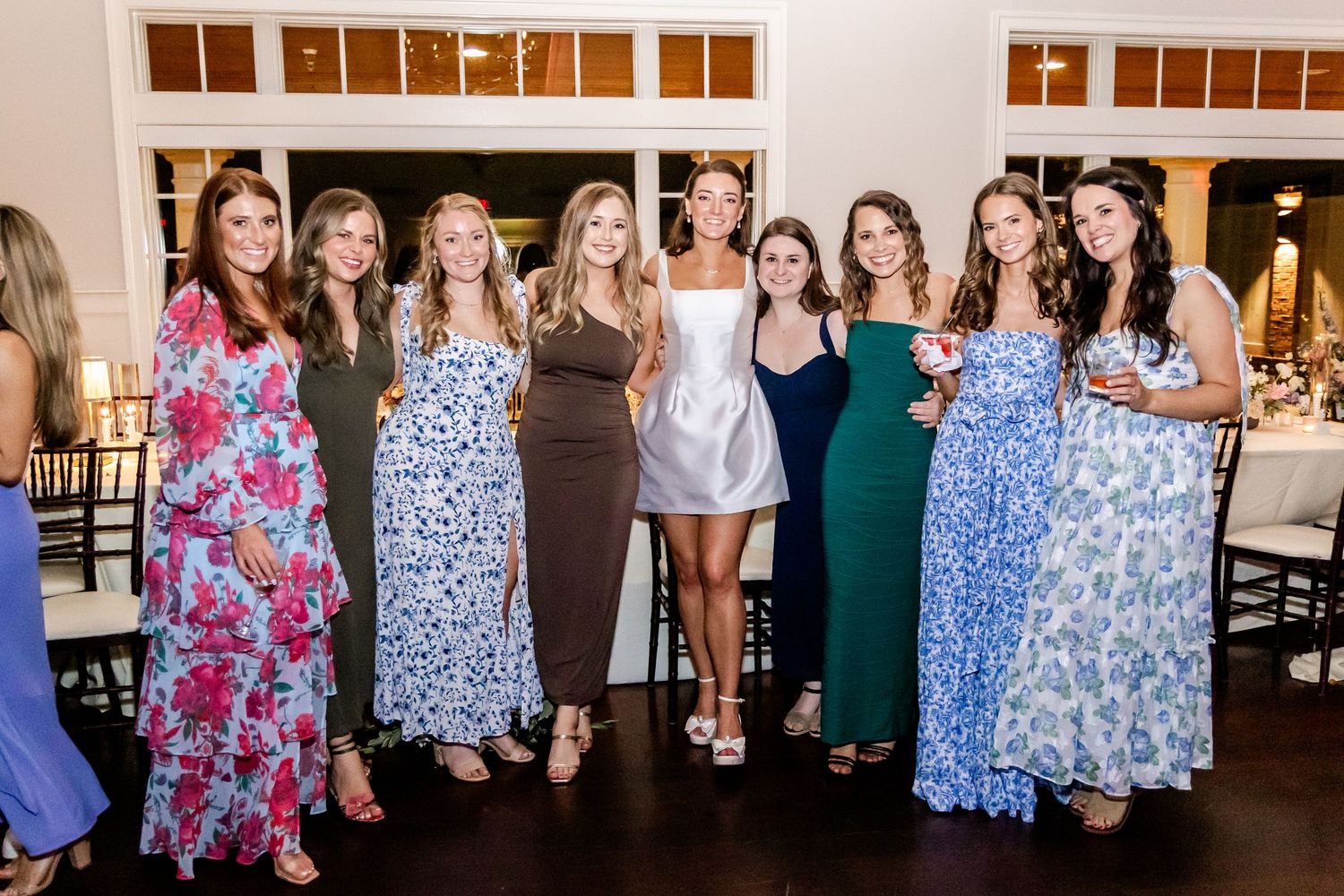 Group of wedding guests in colorful dresses posing together at the reception.
