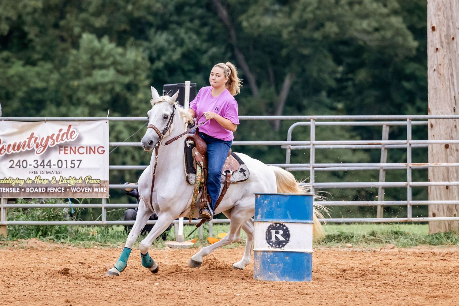 Horse and rider team performing barrel racing drills on a sunny day at a fenced practice arena.