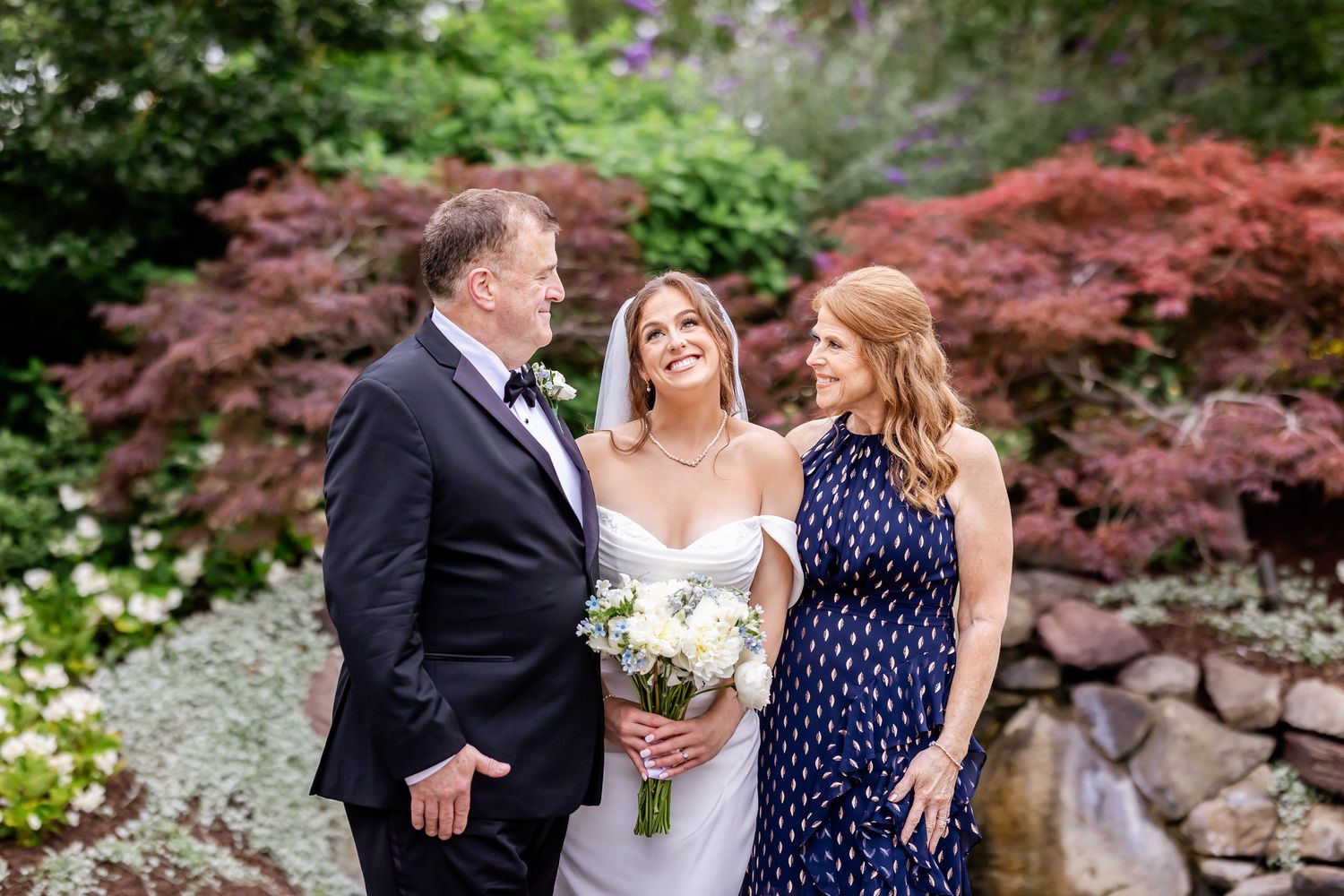 A wedding party poses in front of vibrant Japanese maple trees and garden landscaping.