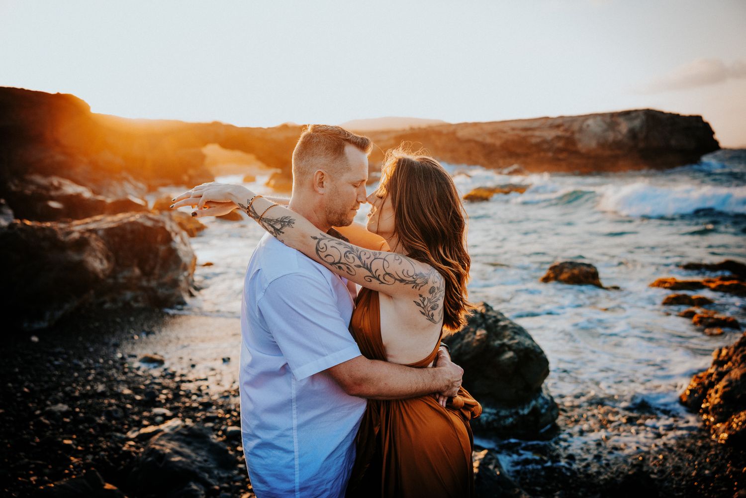 Couple embraces on a rocky beach during golden hour sunset.