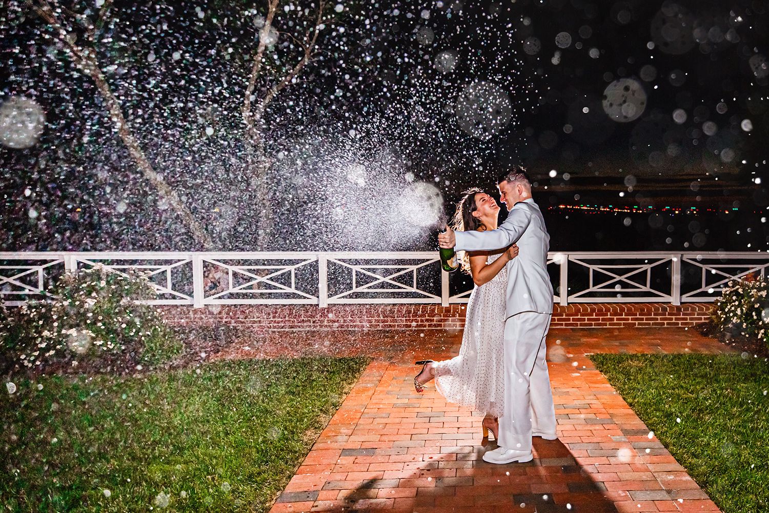 Couple embraces on a brick path during a magical nighttime celebration with sparkling water droplets in the air.