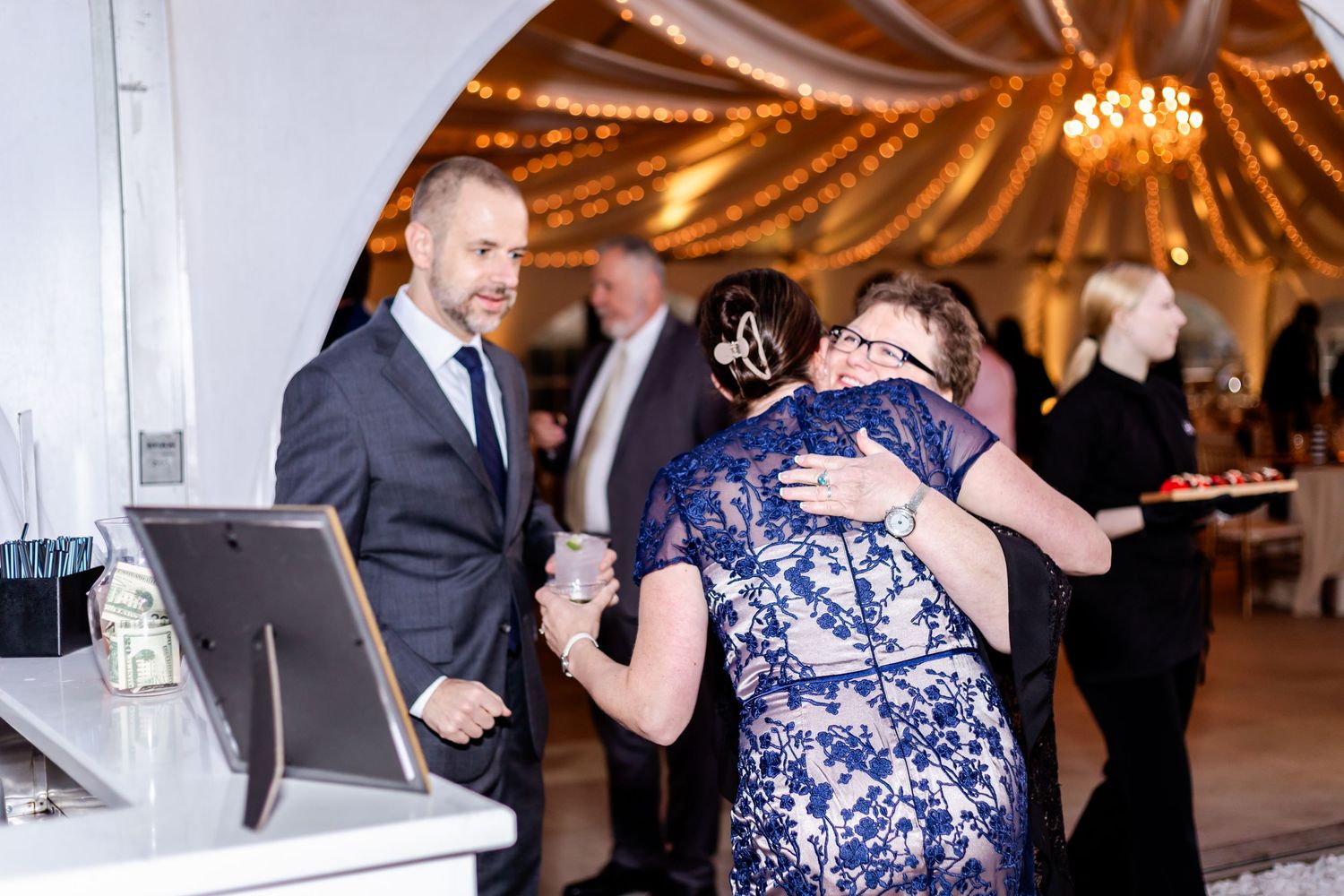 Guests dancing and celebrating inside an elegantly lit white tent with hanging chandeliers.