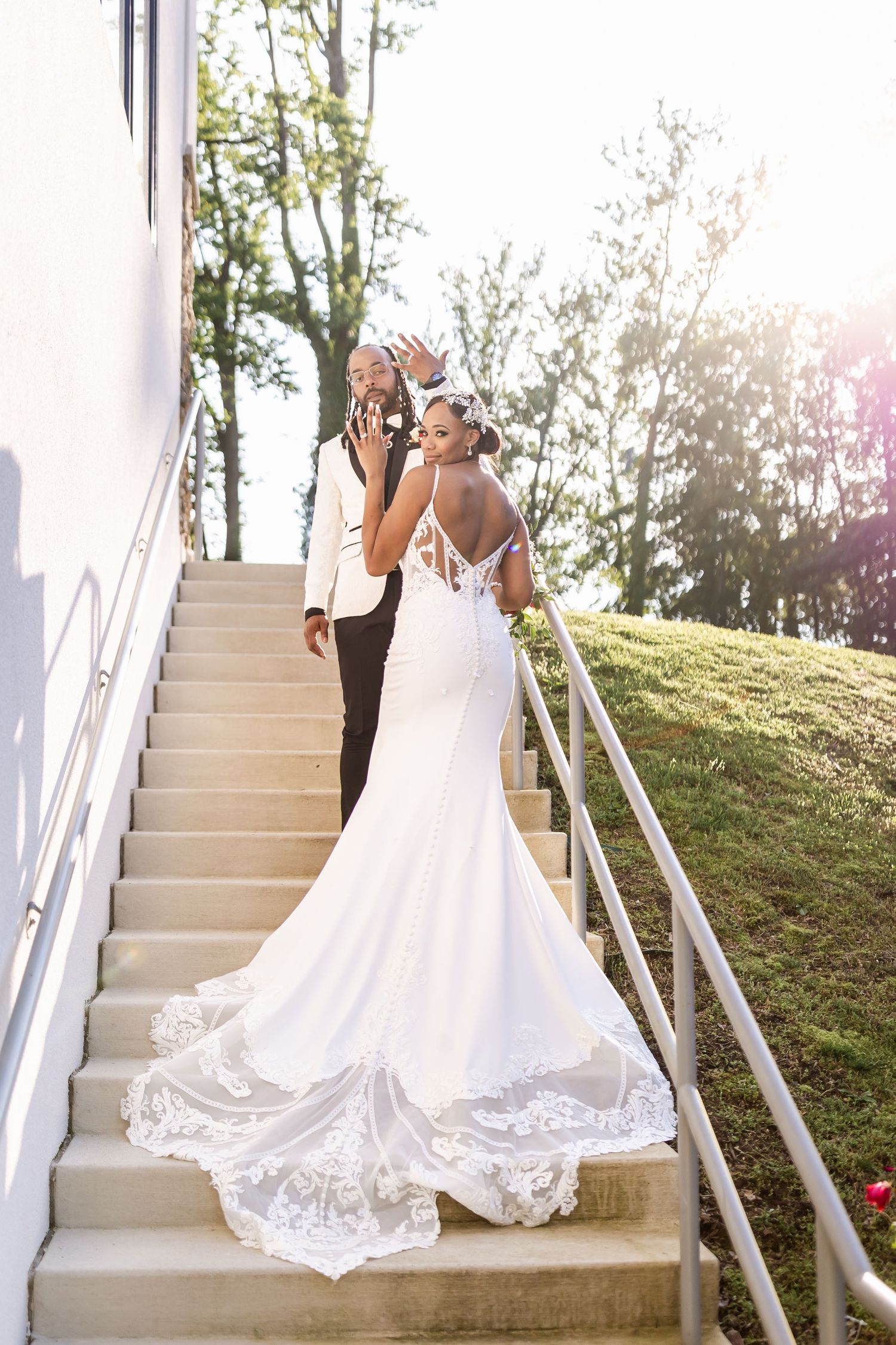 Elegant wedding dress train flowing down white stairs as couple poses together.