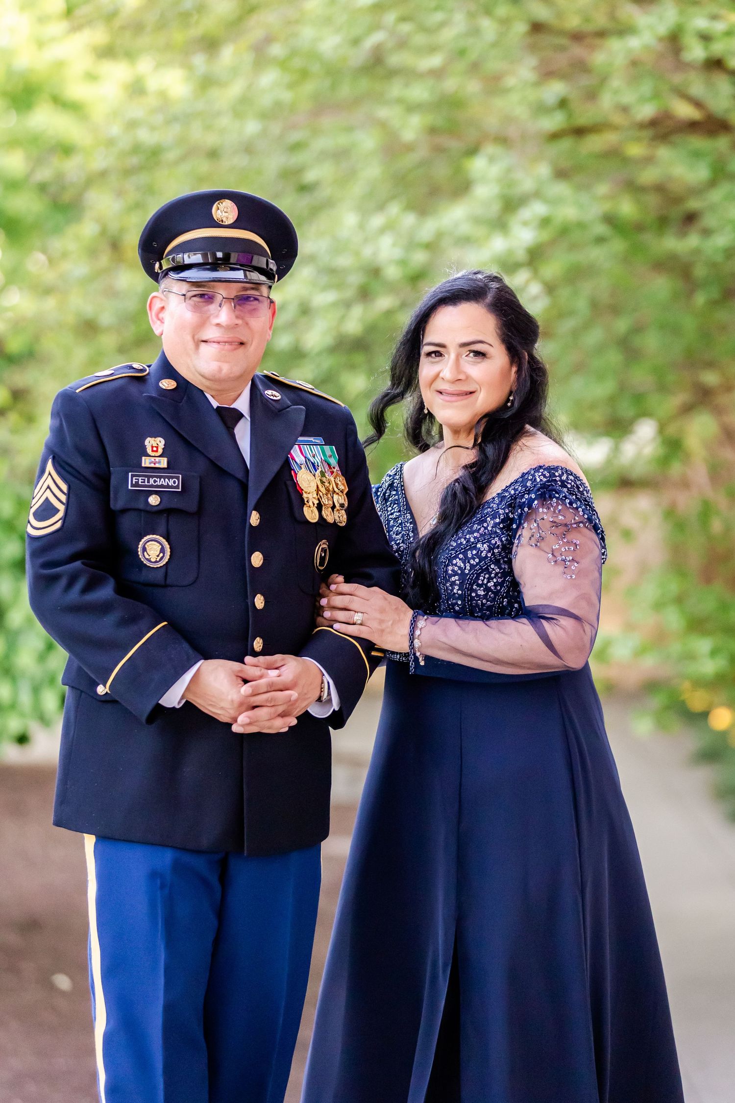 A military servicemember in dress uniform poses with a companion in a navy blue evening gown.
