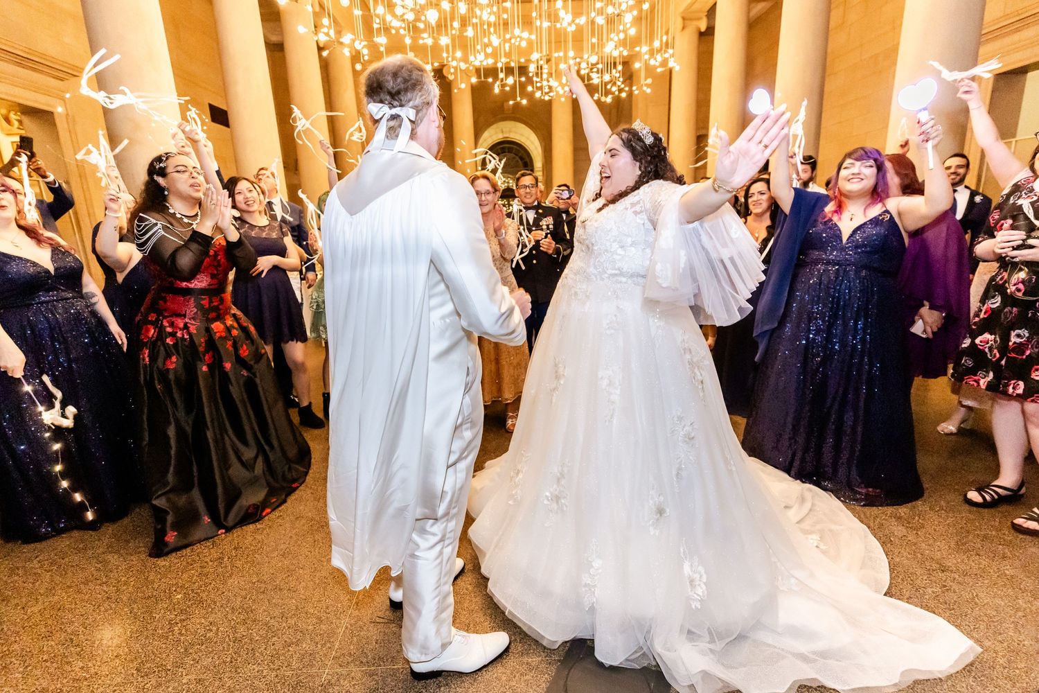 Newlyweds celebrate with guests in an elegant ballroom under chandeliers during their wedding reception.