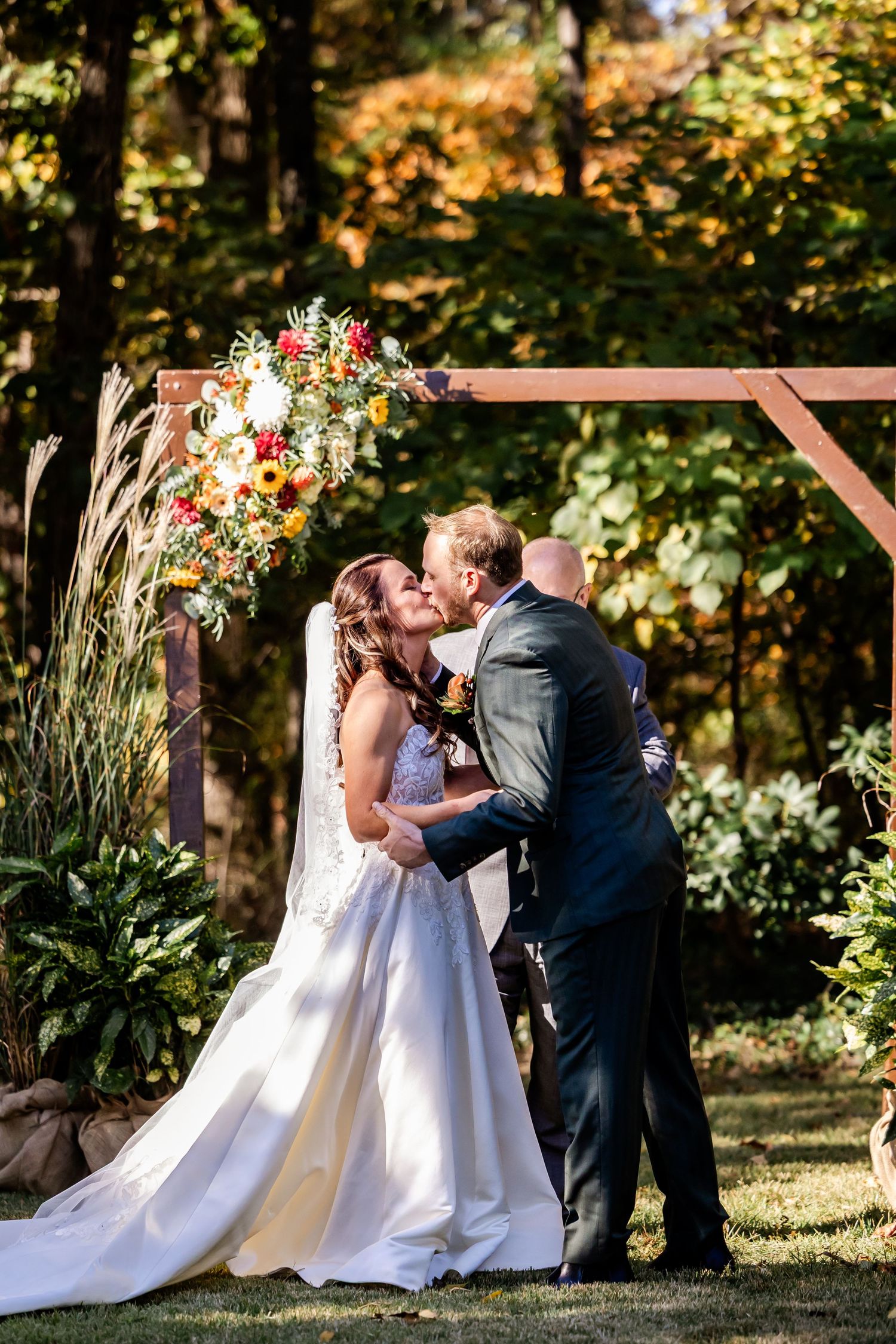 A wedding ceremony under a floral arch during autumn with fall foliage in the background.