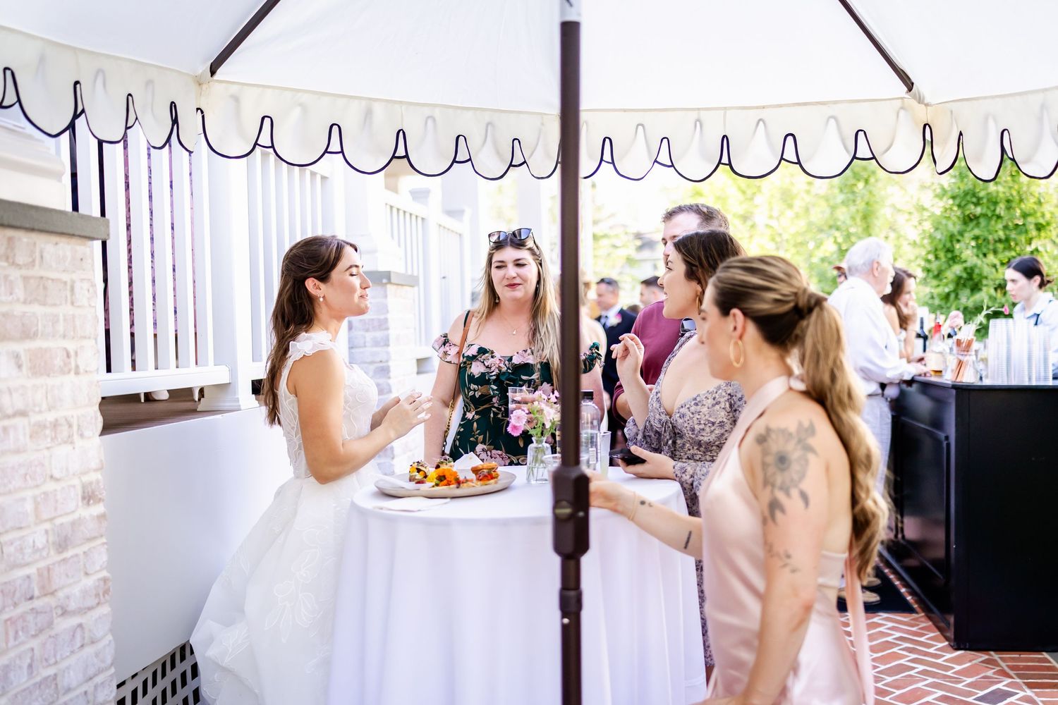 Reception gathering under white tent with guests at cocktail tables.