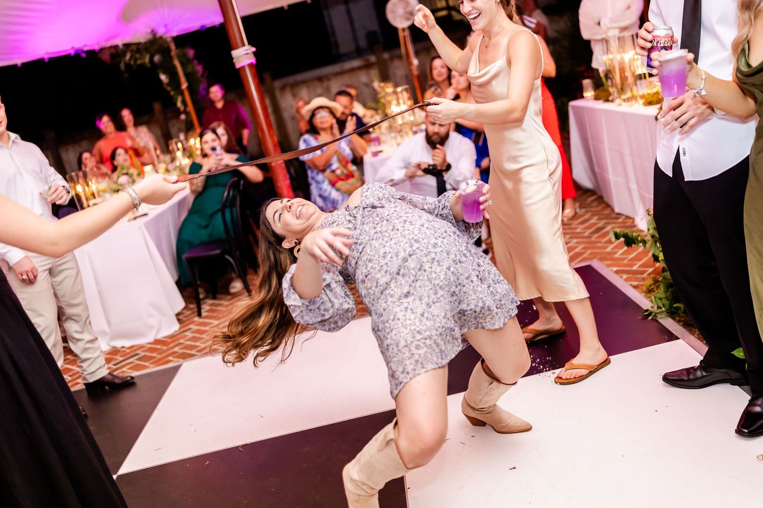 Wedding reception dance floor filled with guests enjoying themselves under pink and purple lighting.