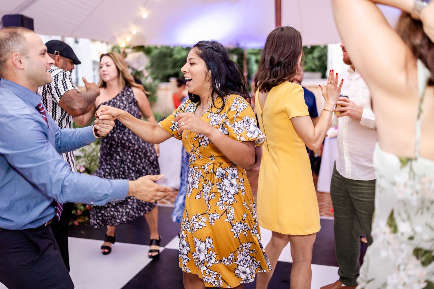 Wedding reception guests dancing and socializing under purple lighting.