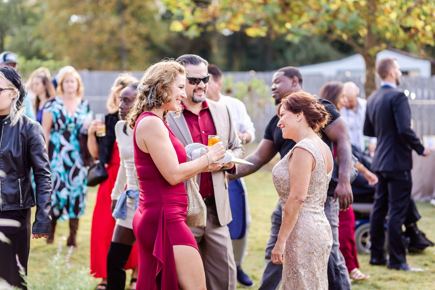 Wedding guests in formal attire dance together at an outdoor reception.