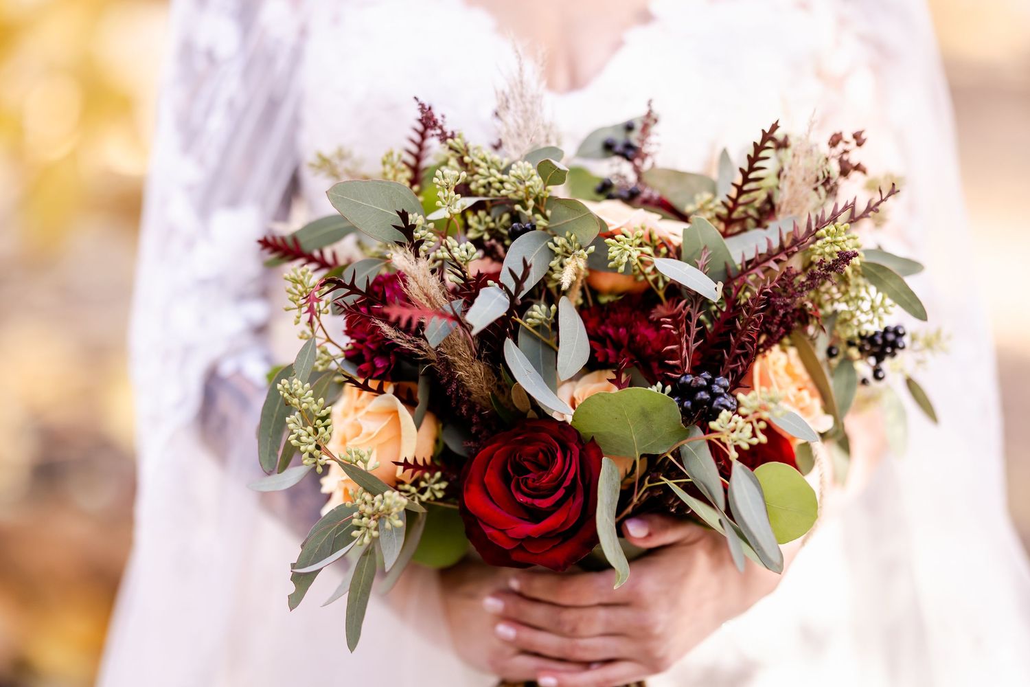 Wedding bouquet details featuring deep red roses, white flowers, and eucalyptus greenery in soft natural light.