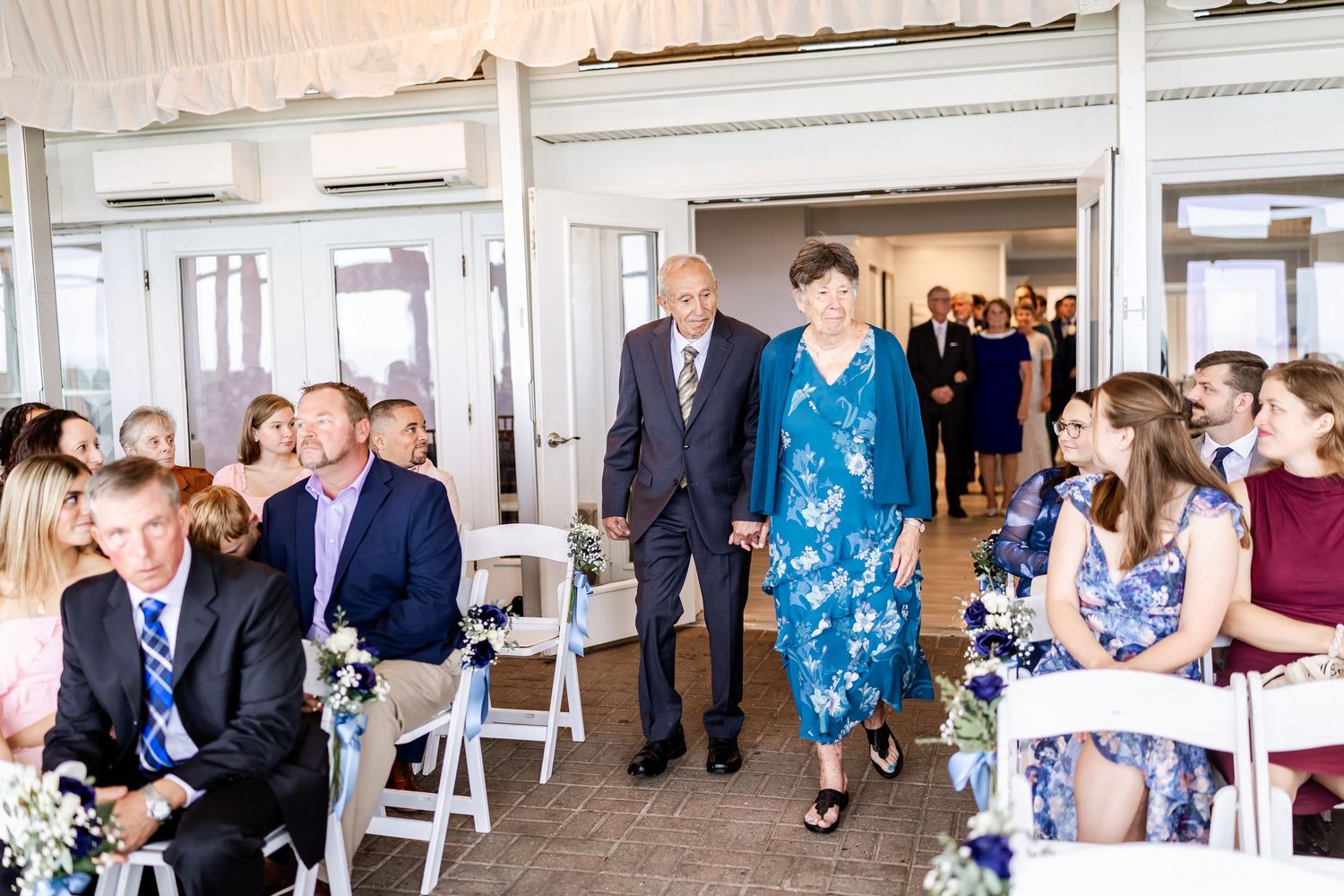 Wedding guests mingle and walk through an elegant white-walled venue hallway.