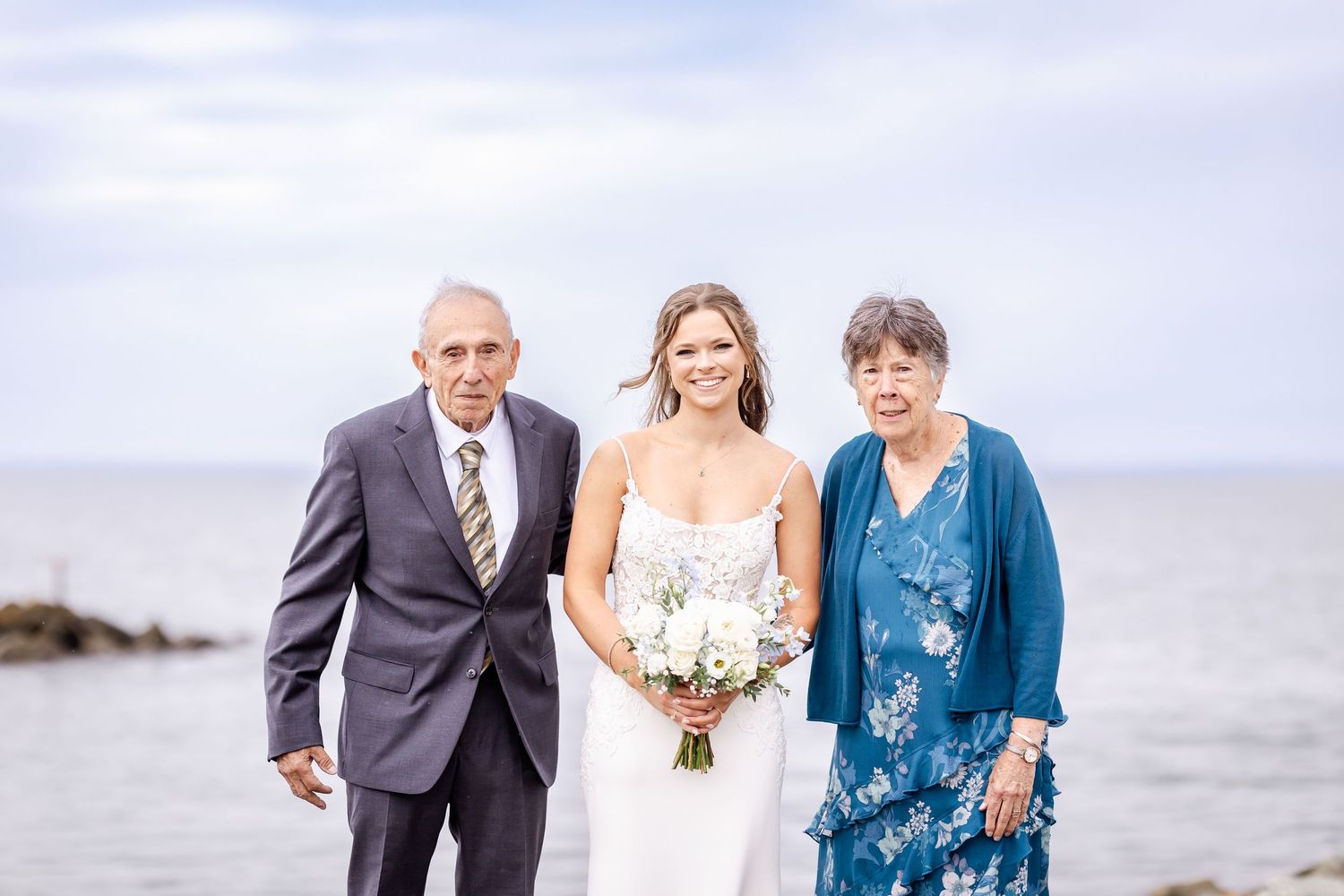 Wedding party members share joyful moments together on a cloudy beach during a seaside celebration.