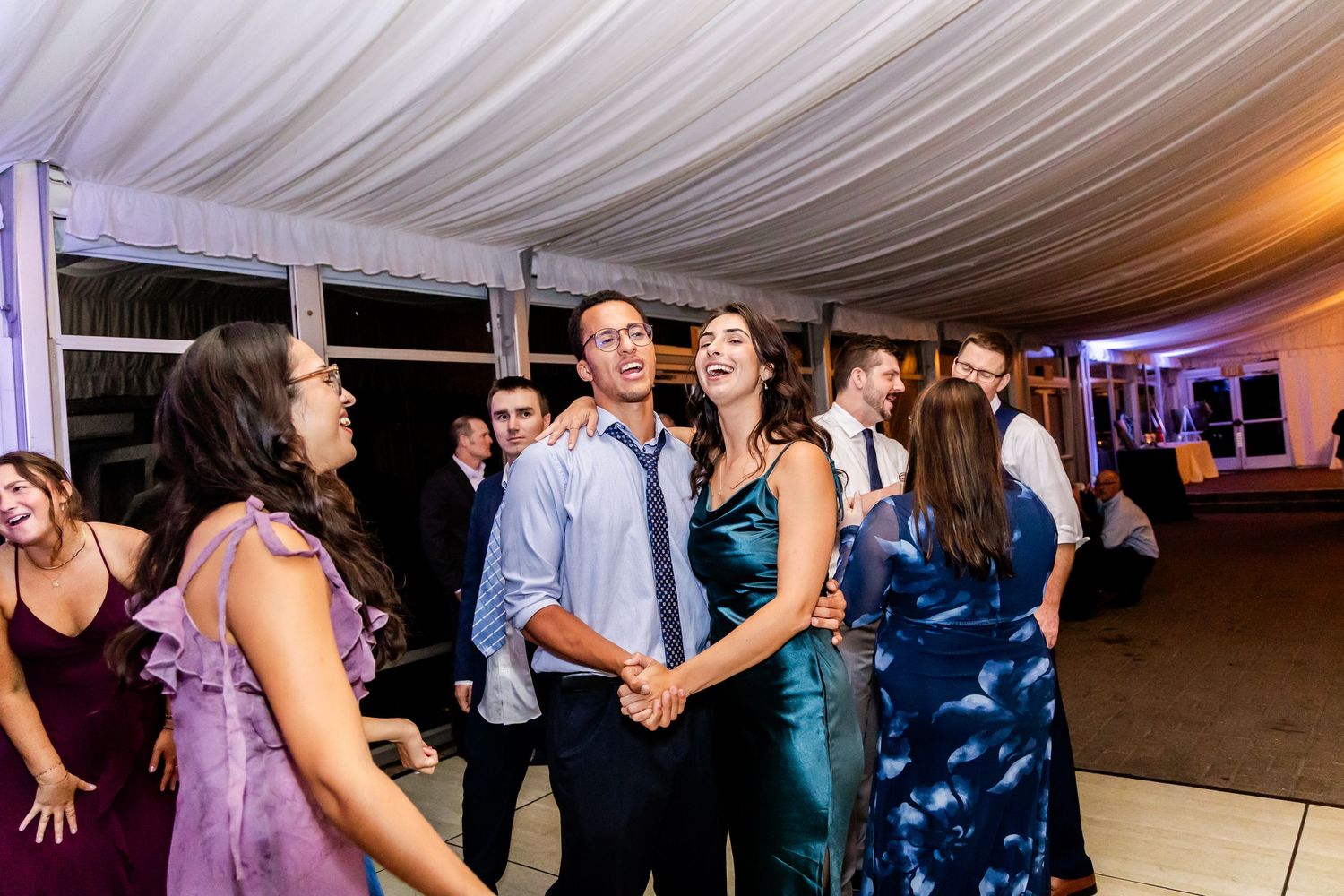 Wedding reception dance floor filled with guests celebrating under draped white ceiling.