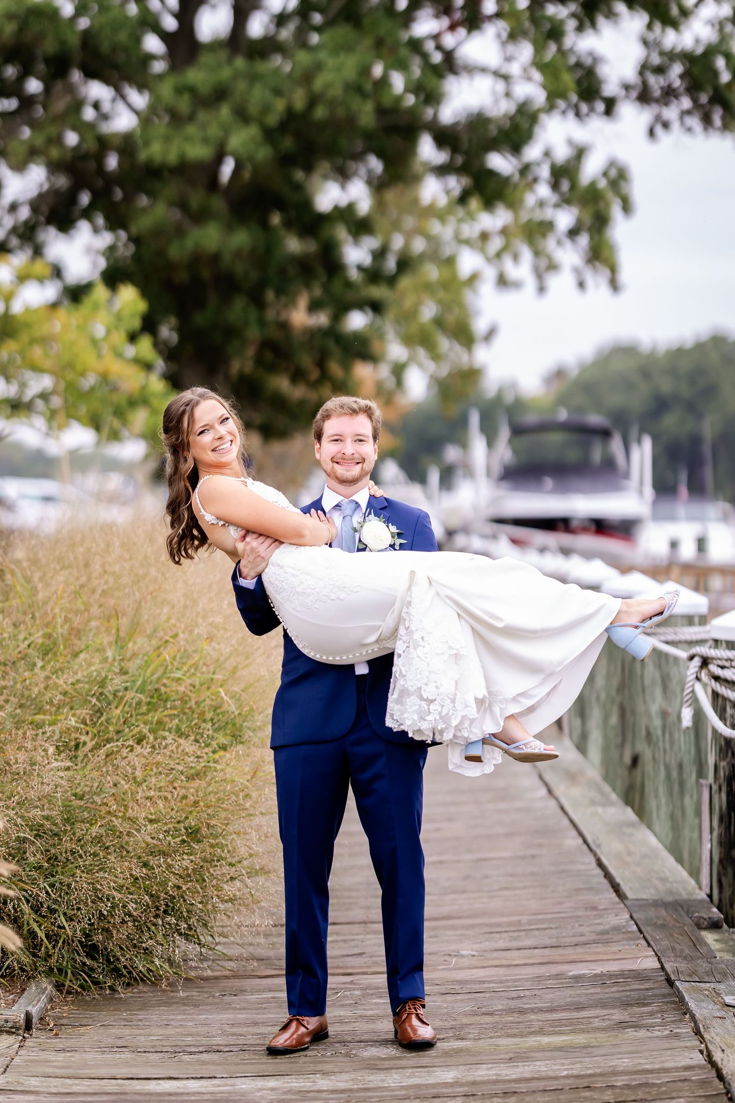 Wedding couple performing playful dip pose sequence on wooden boardwalk near marina.
