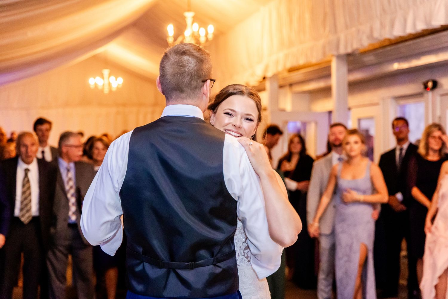 Couple sharing a romantic dance moment under warm chandelier lighting at reception.