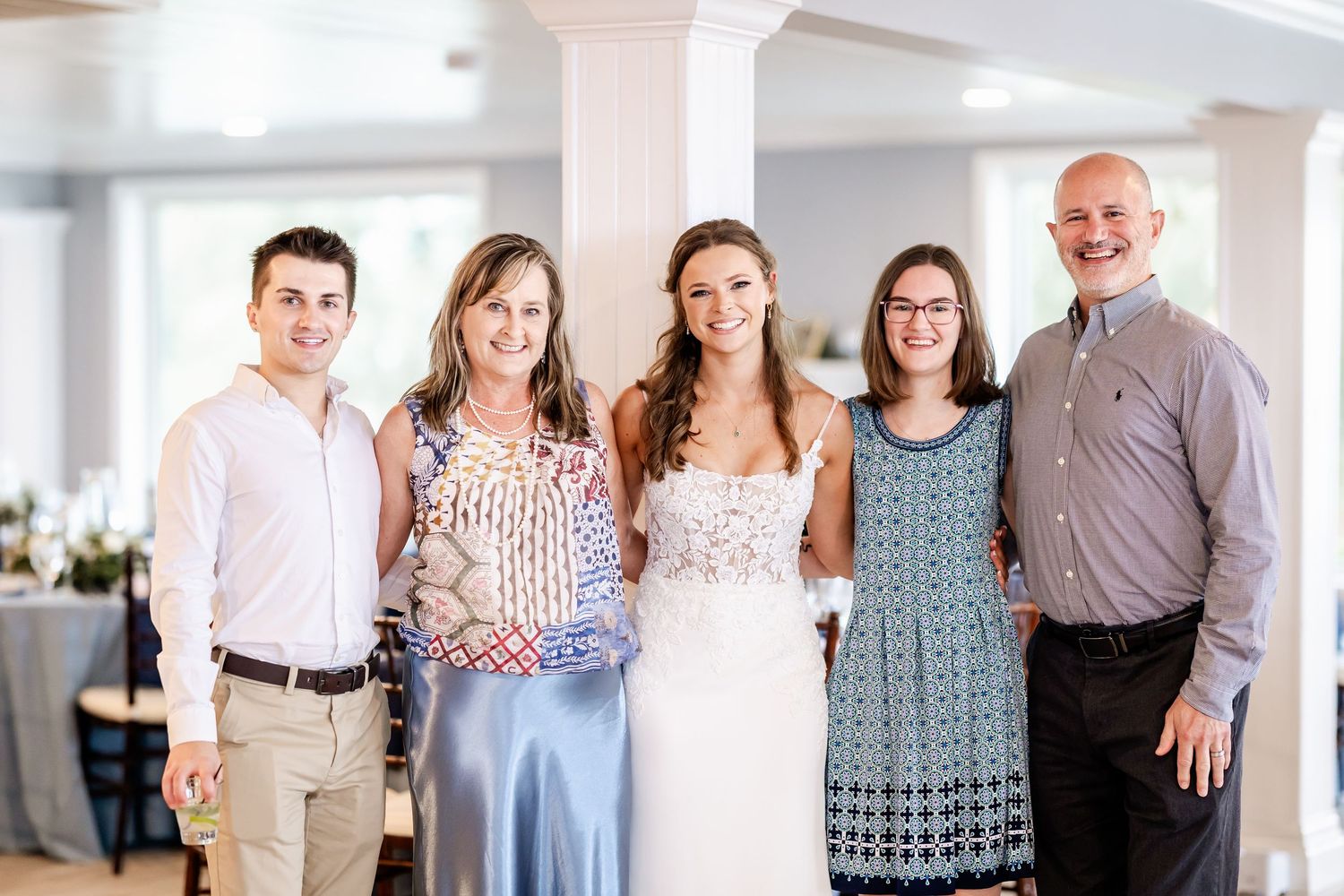 Group of wedding guests pose together in a bright indoor venue with white columns.
