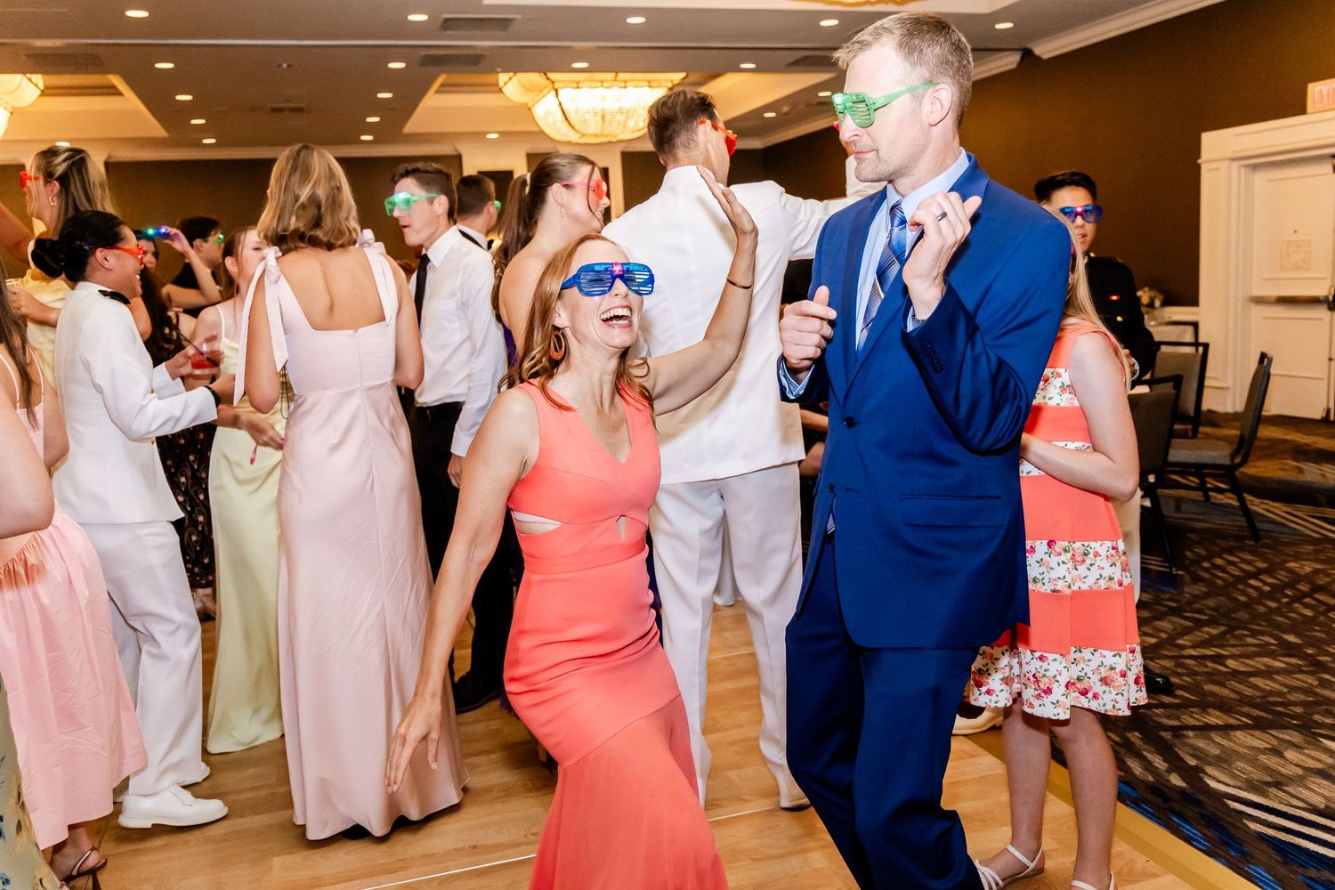 Wedding guests dancing and celebrating in formal attire at a reception venue.