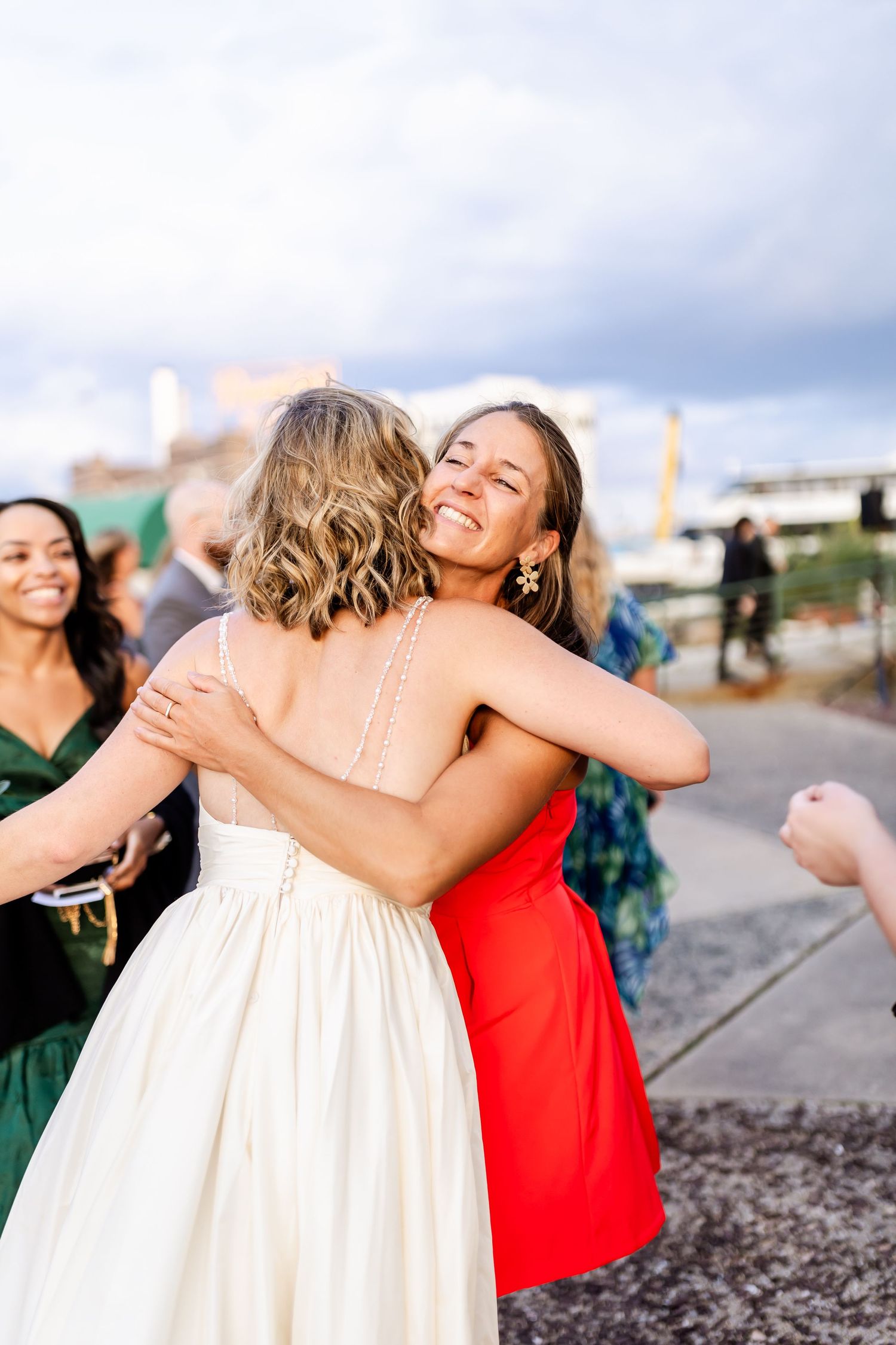 Two wedding guests share a joyful embrace outdoors on a sunny day.