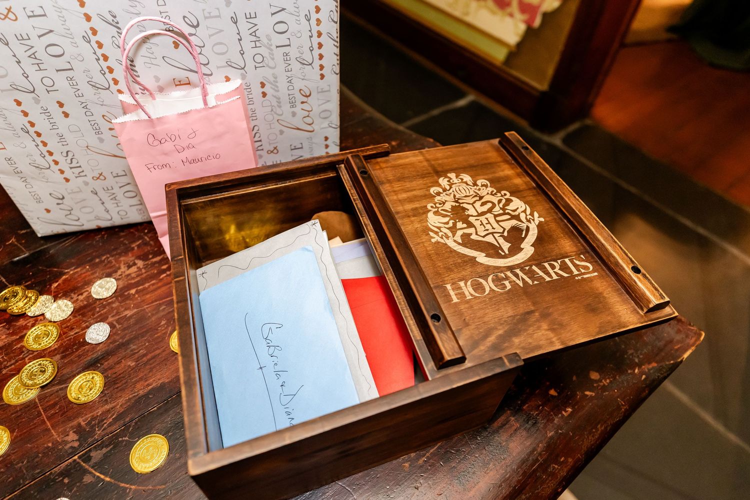Decorative wooden box with Hogwarts crest and pink gift bag on aged surface.