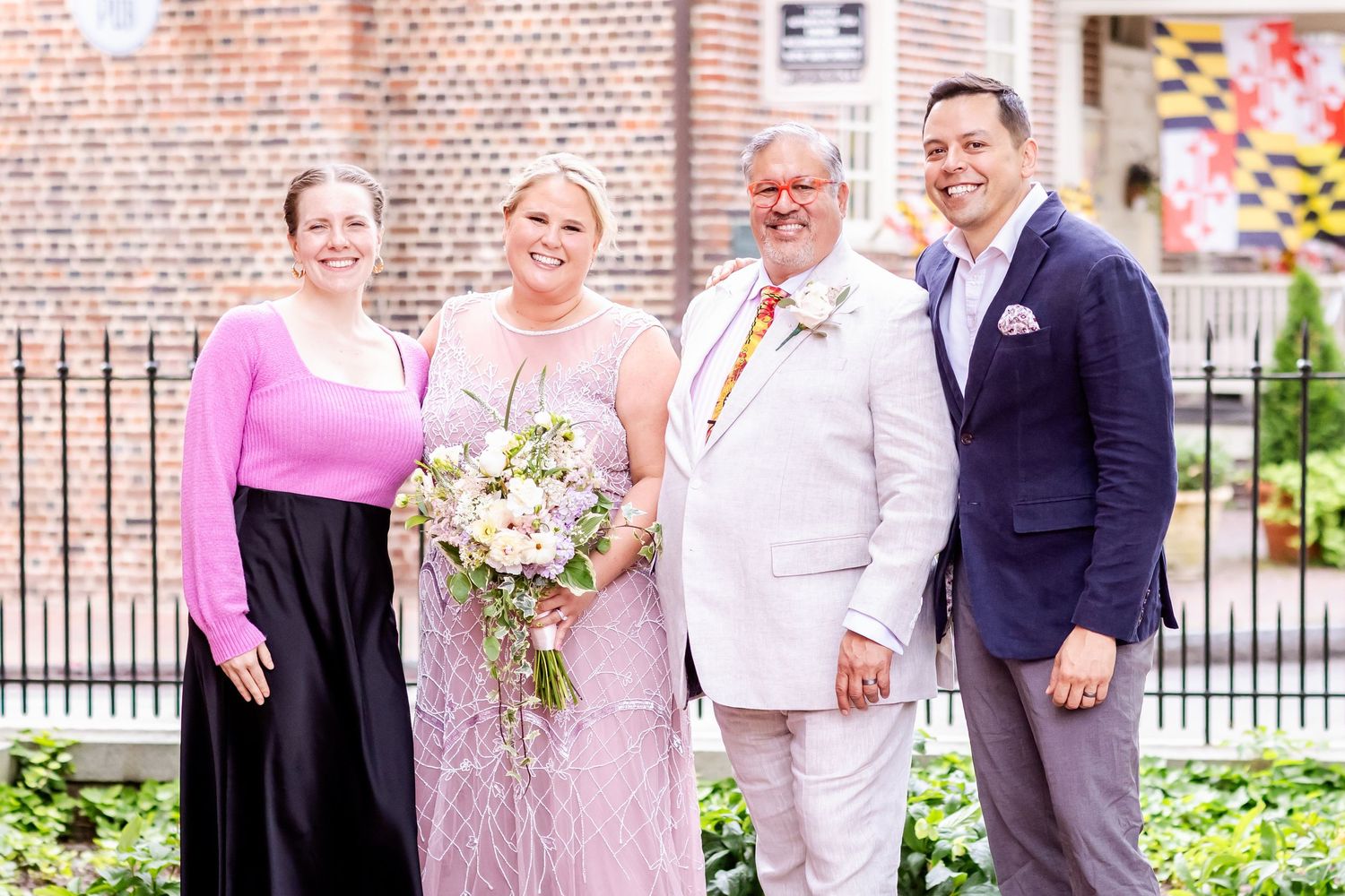 Formal wedding portrait outside historic brick building with garden landscaping.