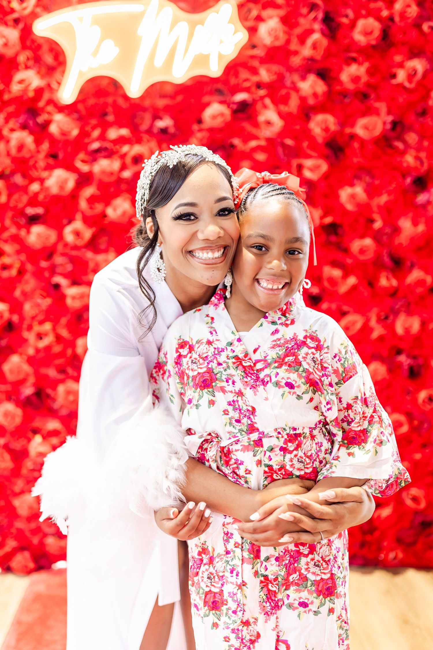 Portrait against vibrant red flower wall backdrop in white and floral pattern dresses.