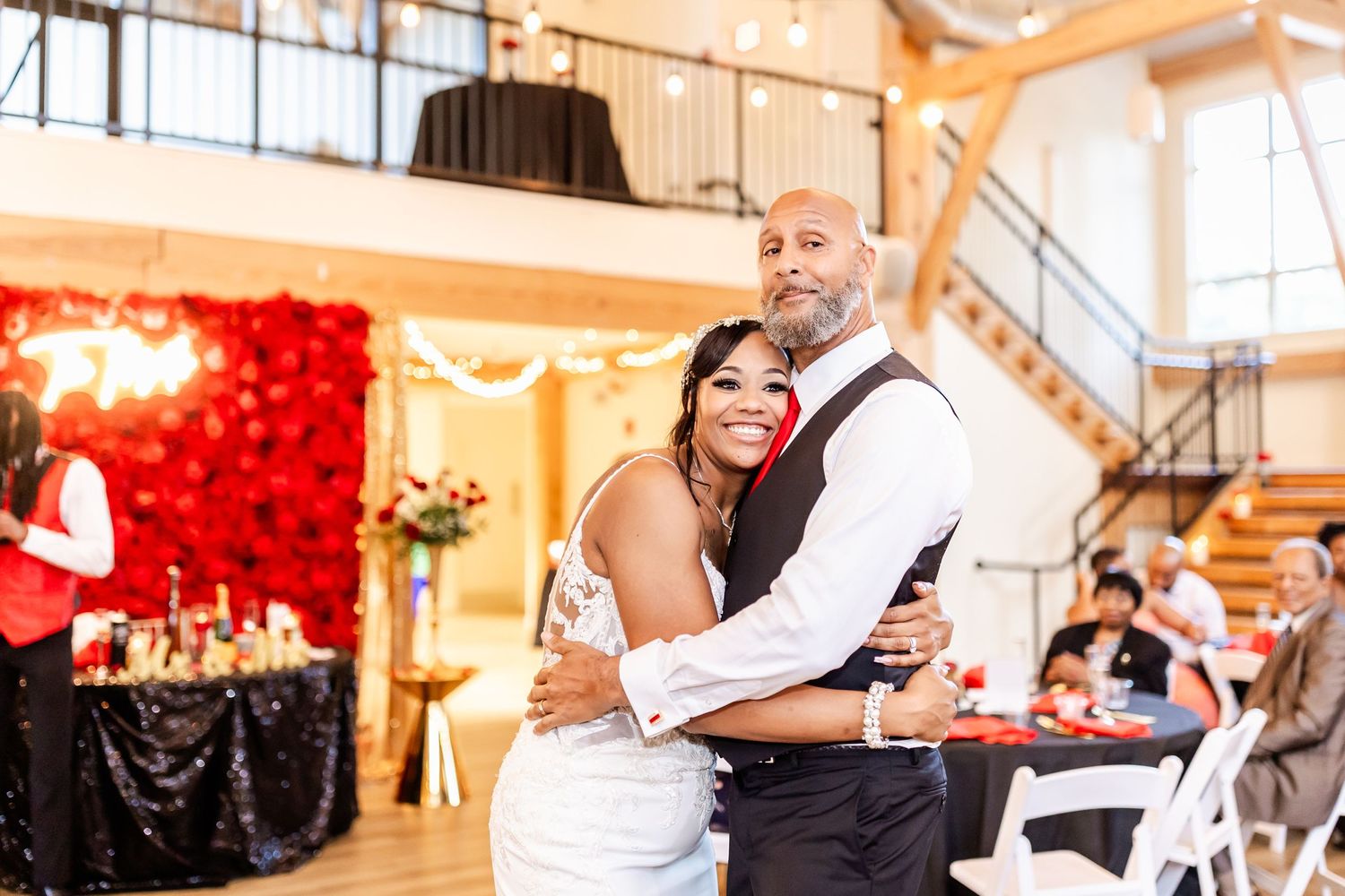 Romantic moment during wedding reception with red rose wall and elegant decor.
