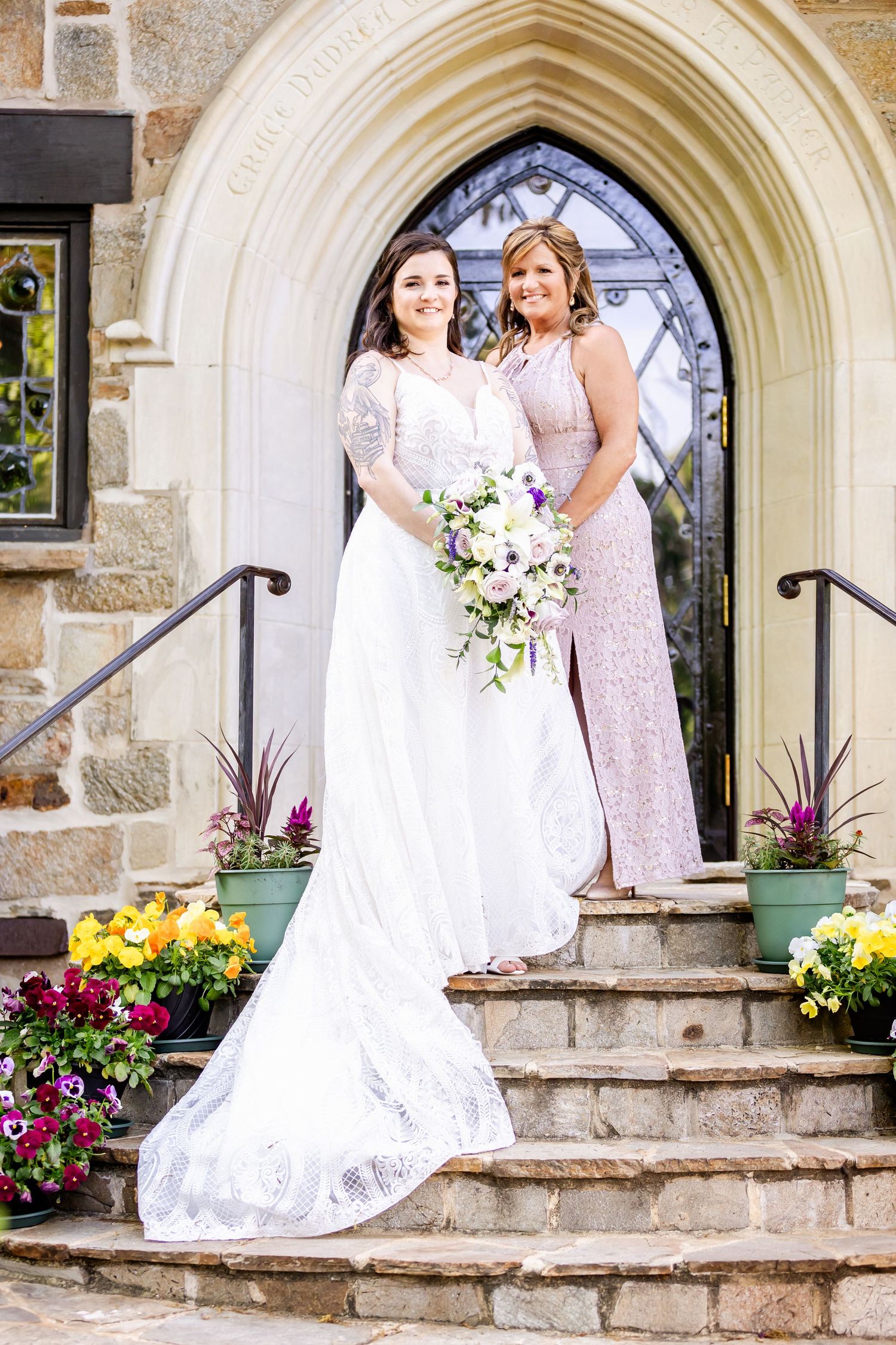 Elegant bridal photo on stone church steps decorated with colorful flowers and gothic archway.