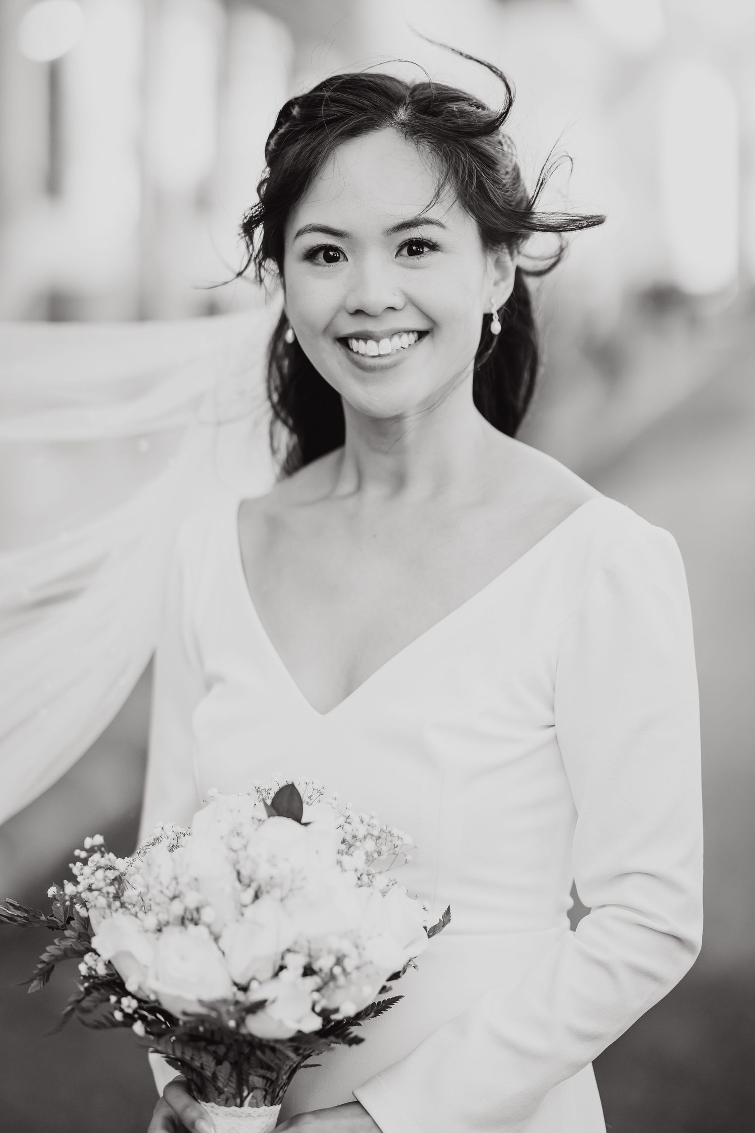 Elegant bride in classic white v-neck dress holding bouquet in black and white portrait.