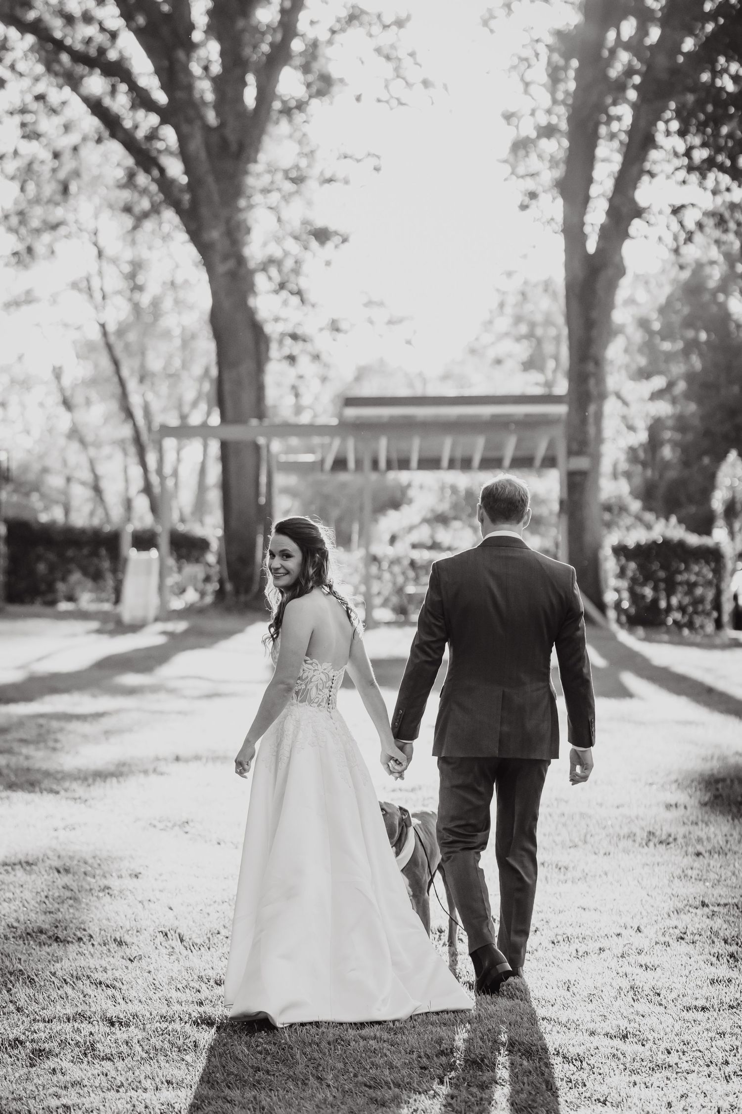 A black and white photo of a couple walking together on a tree-lined path.