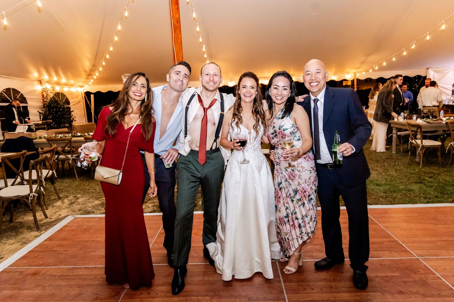 Wedding reception guests dancing under a white tent with warm string lights.