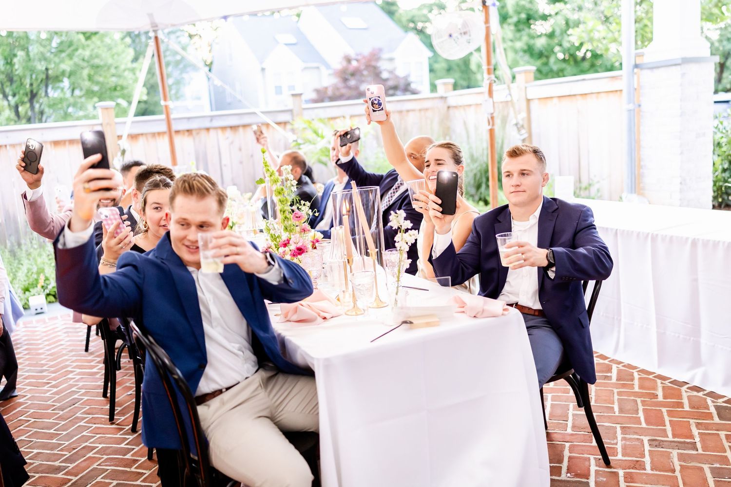 Wedding party members dance and celebrate on a brick patio during an outdoor reception.