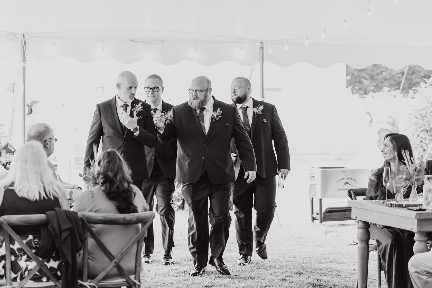 A black and white photo of groomsmen walking together at an outdoor wedding ceremony.