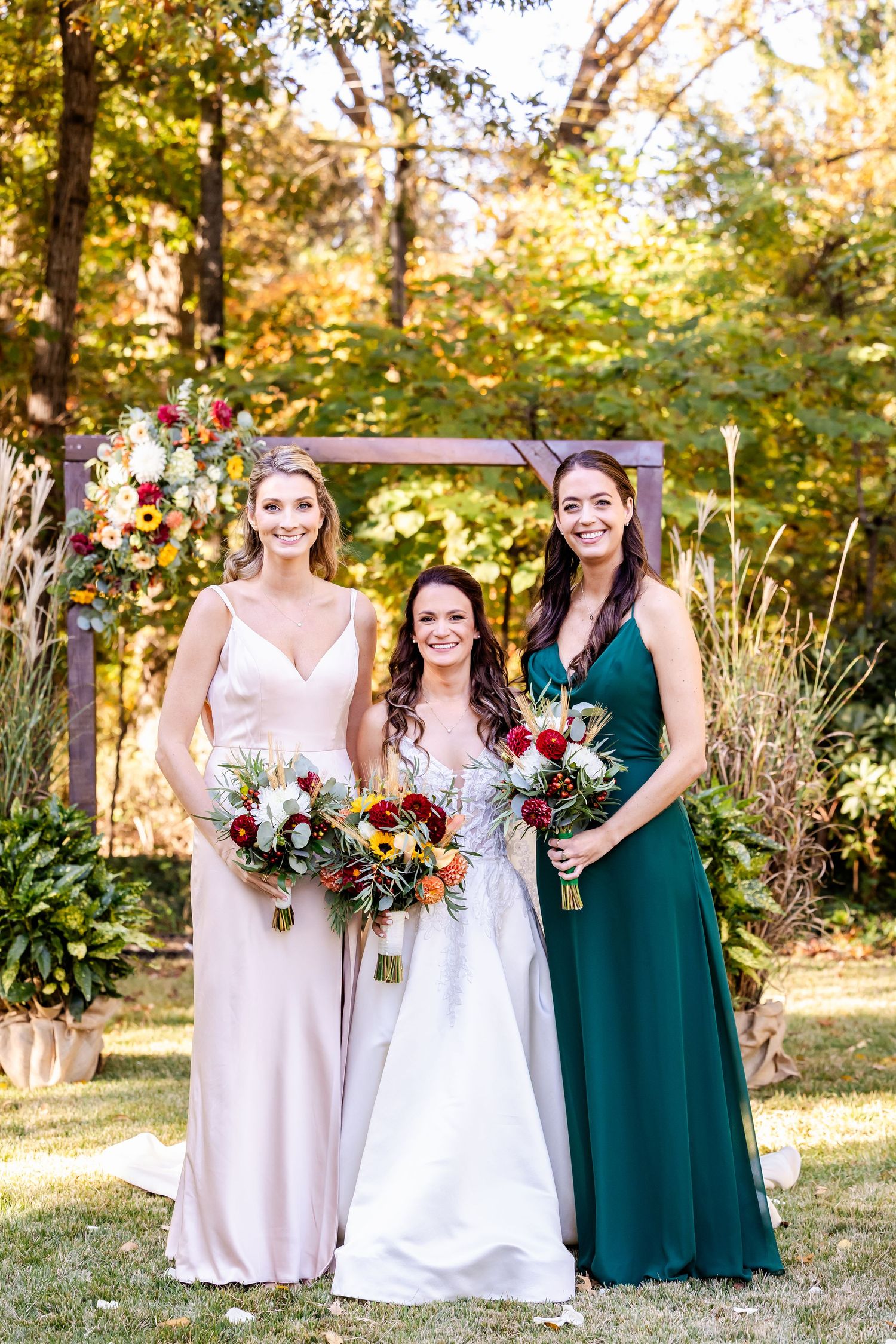 Wedding party poses outdoors in autumn with bridesmaids wearing emerald green and blush pink gowns.